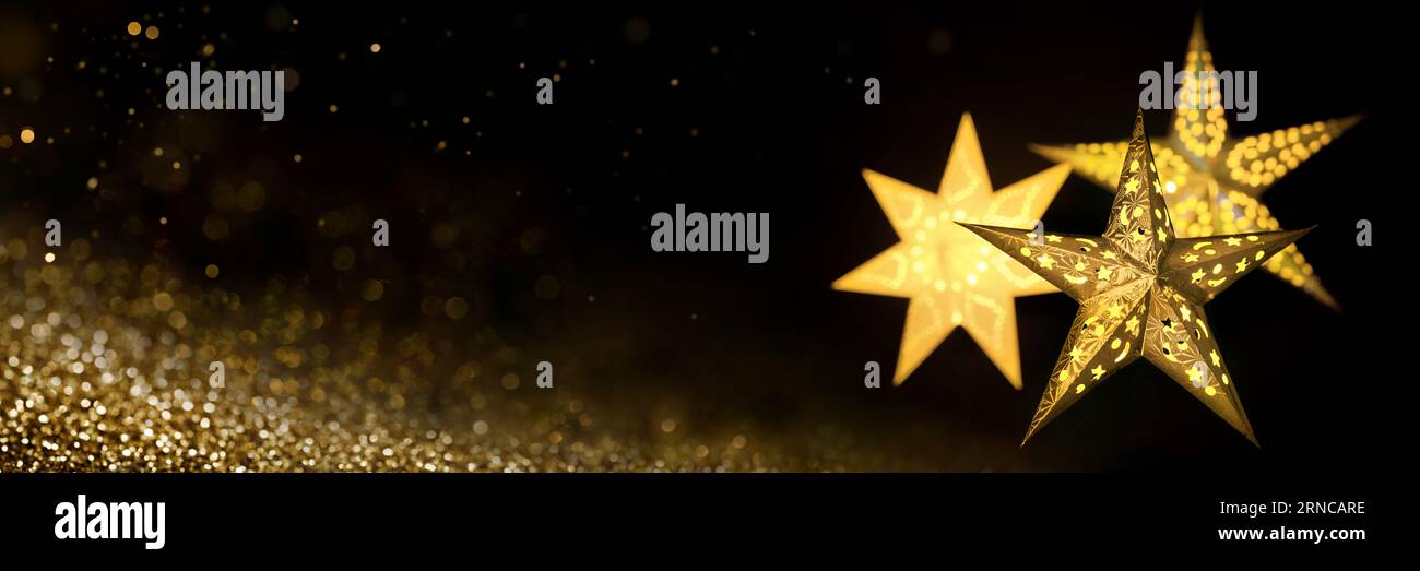 Verzierte goldene Sternlaternen für Weihnachten auf schwarzem Hintergrund mit goldenem Sternenstaub, extra breites Format mit Kopierraum Stockfoto