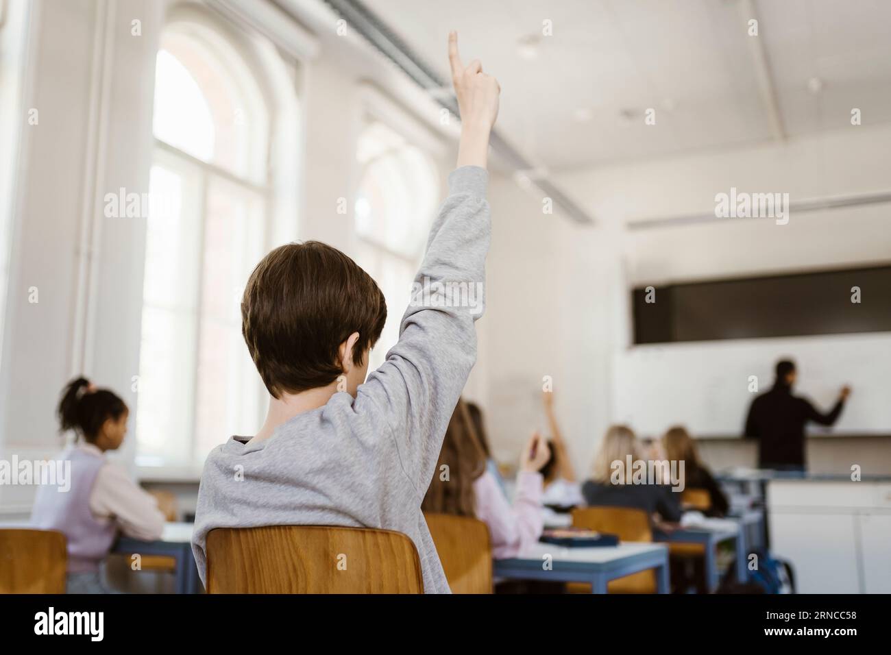 Junge, der die Hand hebt, während er Vorlesungen im Klassenzimmer besucht Stockfoto
