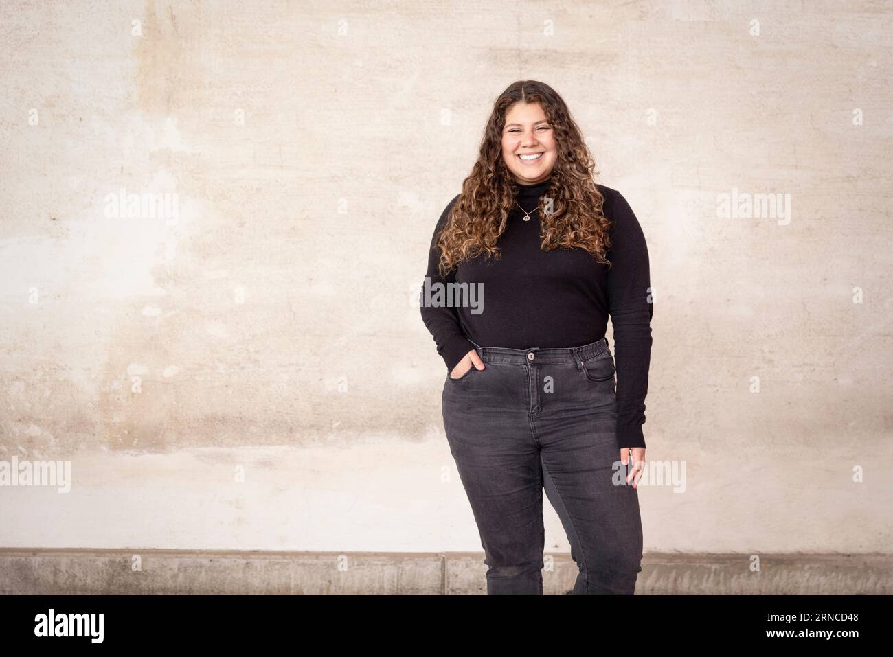 Porträt einer glücklichen Frau mit Hand in der Tasche, die im Recyclingzentrum gegen die Wand steht Stockfoto