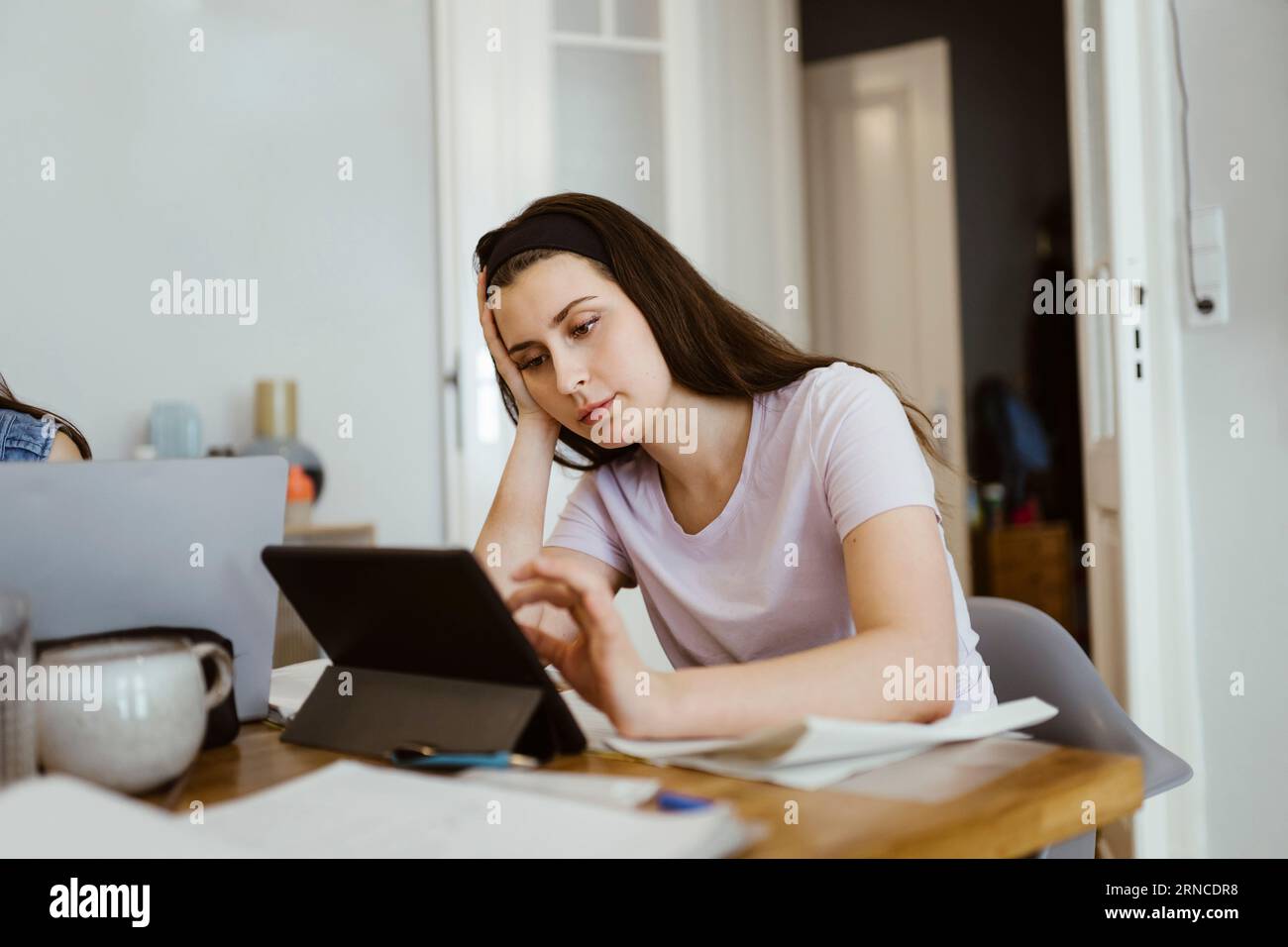 Langweilige junge Frau, die beim Lernen am Tisch ein digitales Tablet verwendete Stockfoto