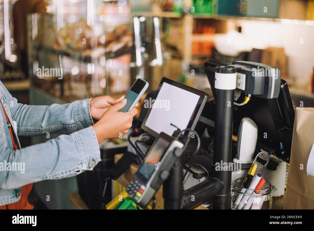 Mitte der Frau, die beim Scannen des QR-Codes zur Bezahlung an der Kasse ein Smartphone verwendet Stockfoto