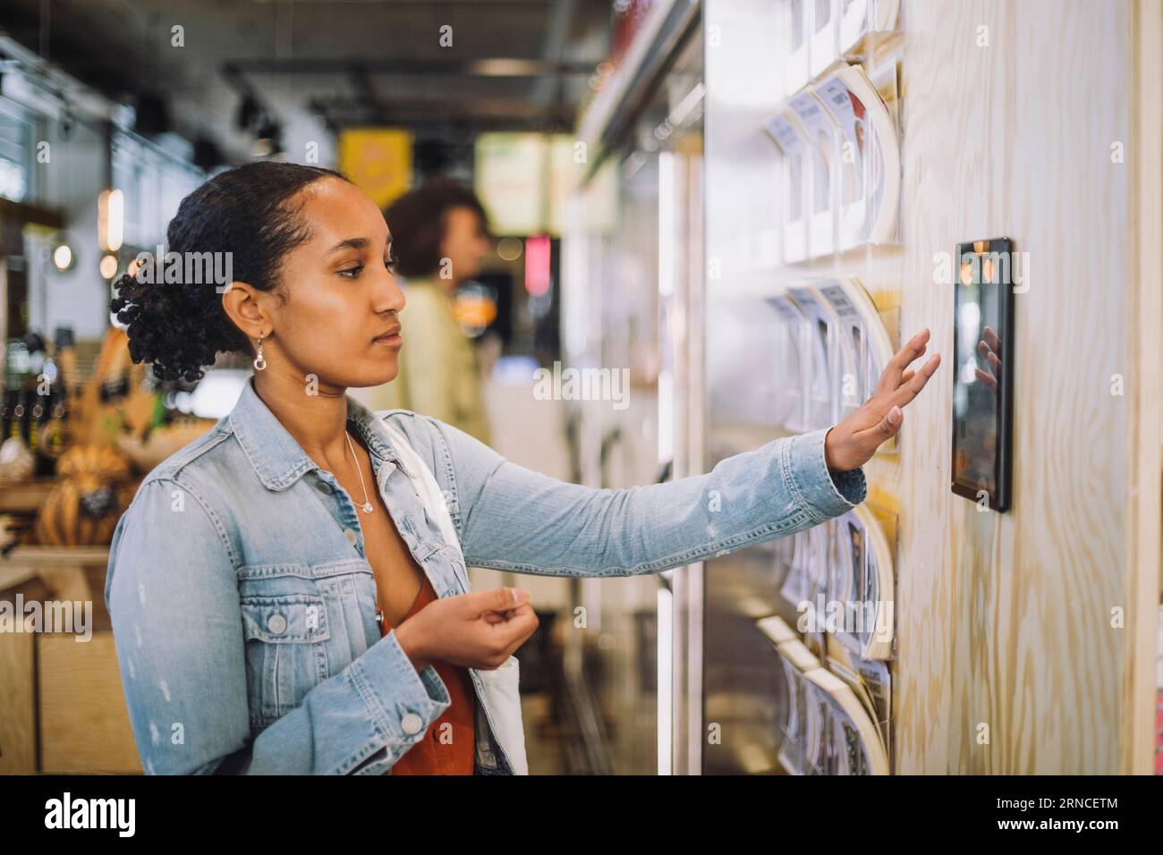 Weibliche Kundin, die ein digitales Tablet im Lebensmittelgeschäft an der Wand montiert hat Stockfoto