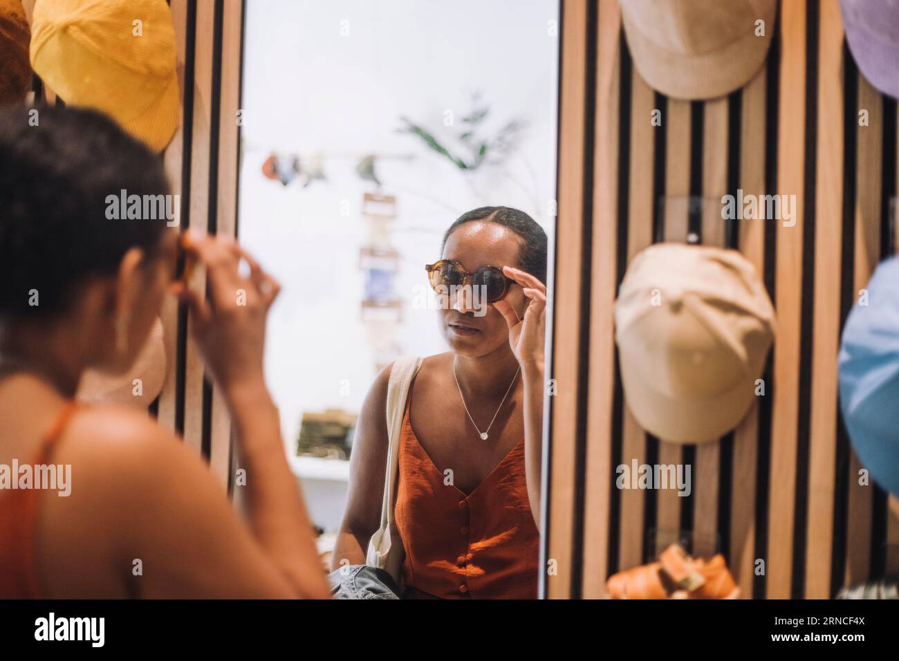 Frau versucht, eine Sonnenbrille zu benutzen, während sie in der Modeboutique auf Reflexion schaut Stockfoto