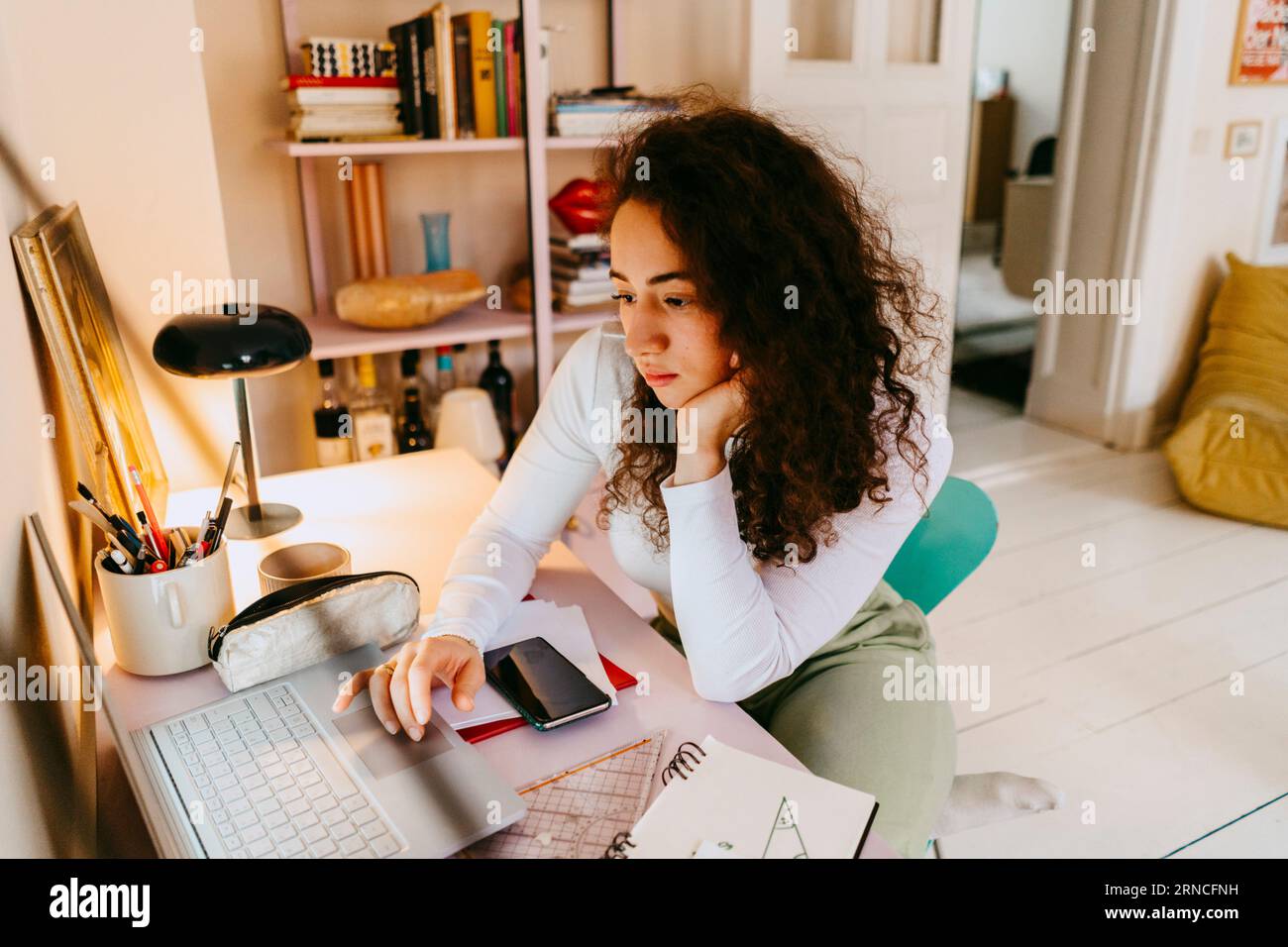 Junge Frau mit lockigem Haar, die während des Studiums zu Hause einen Laptop benutzt Stockfoto