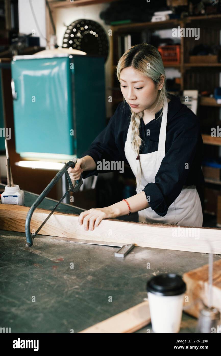 Junge Unternehmerin, die Holz auf der Werkbank schneidet Stockfoto
