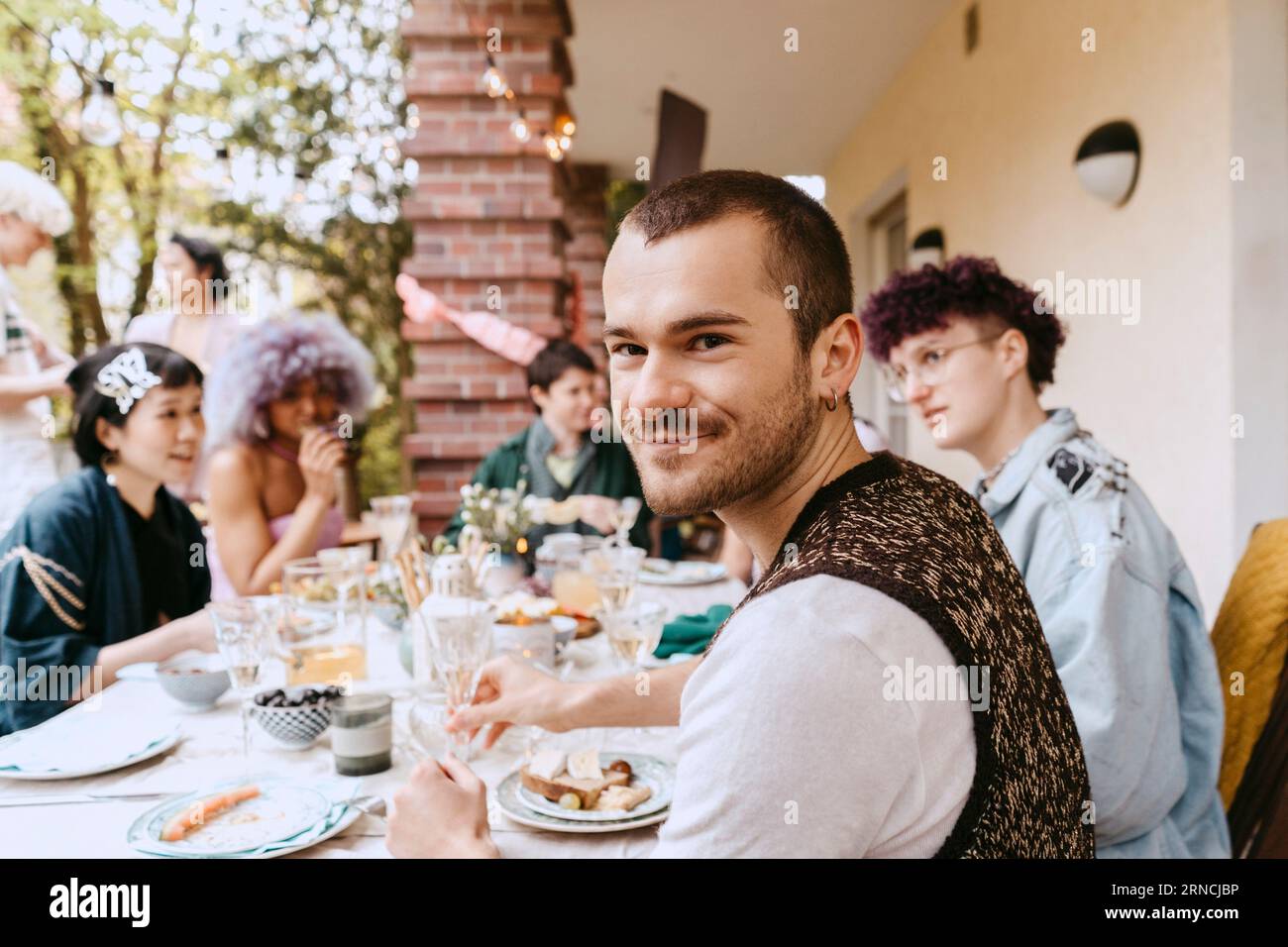 Porträt eines lächelnden schwulen Mannes, der mit LGBTQ-Freunden während einer Dinnerparty im Hinterhof sitzt Stockfoto