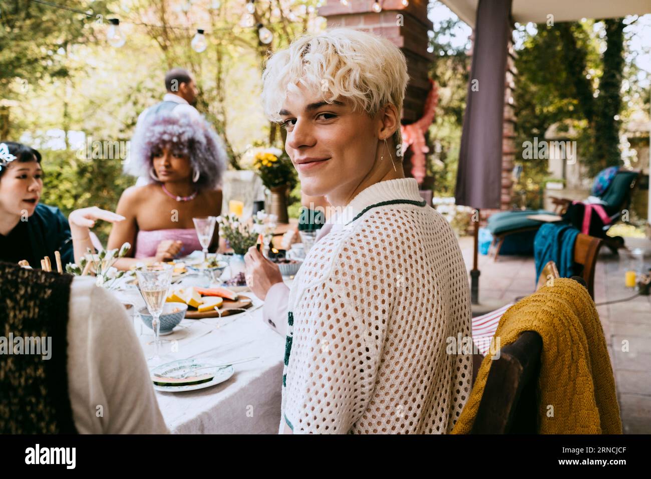 Porträt eines lächelnden schwulen Mannes mit grauen Haaren, der während einer Dinnerparty im Hinterhof unter Freunden sitzt Stockfoto