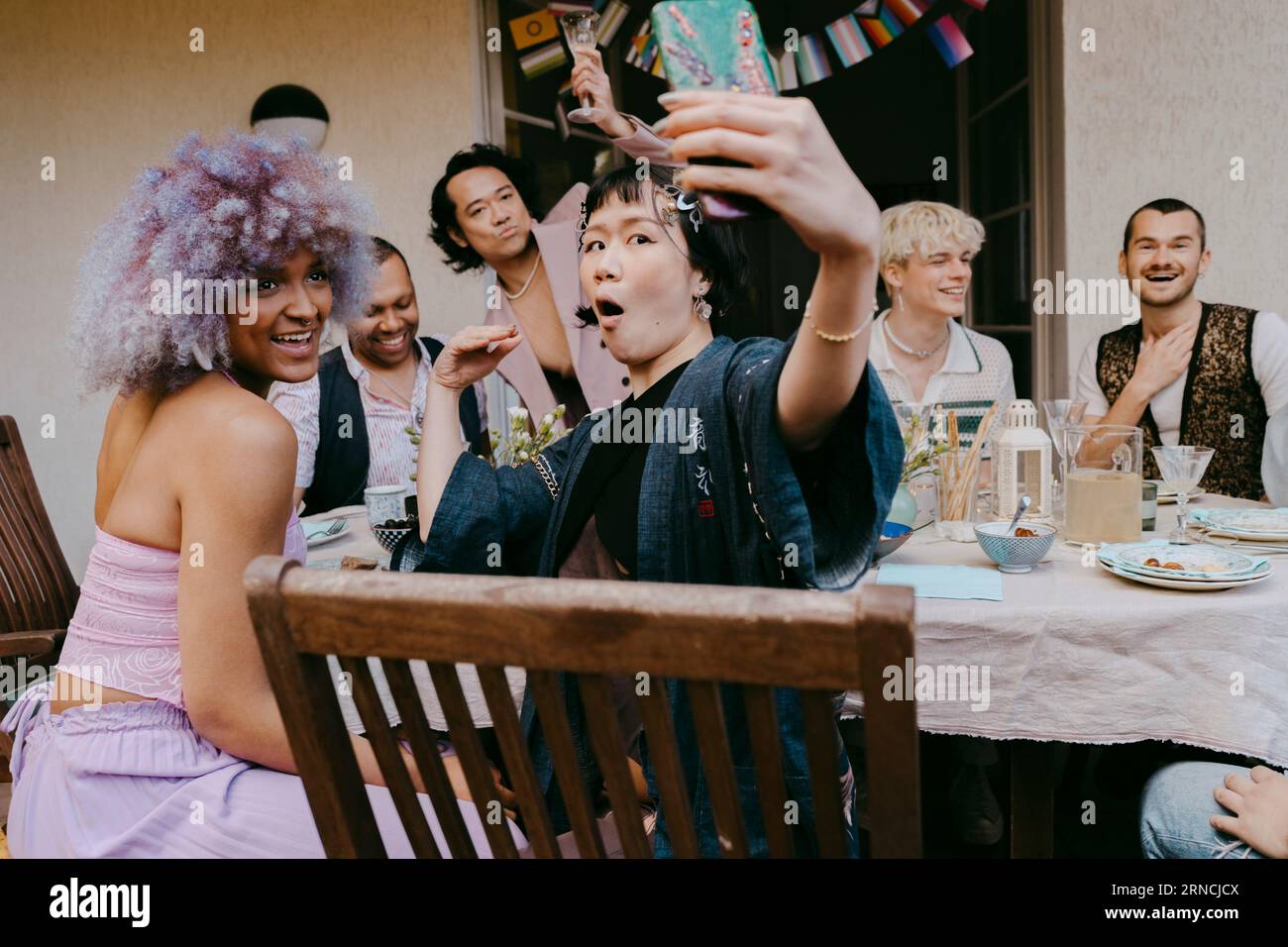 Transwoman nimmt Selfie mit Freunden der LGBTQ-Community auf dem Smartphone während einer Dinnerparty im Hinterhof Stockfoto