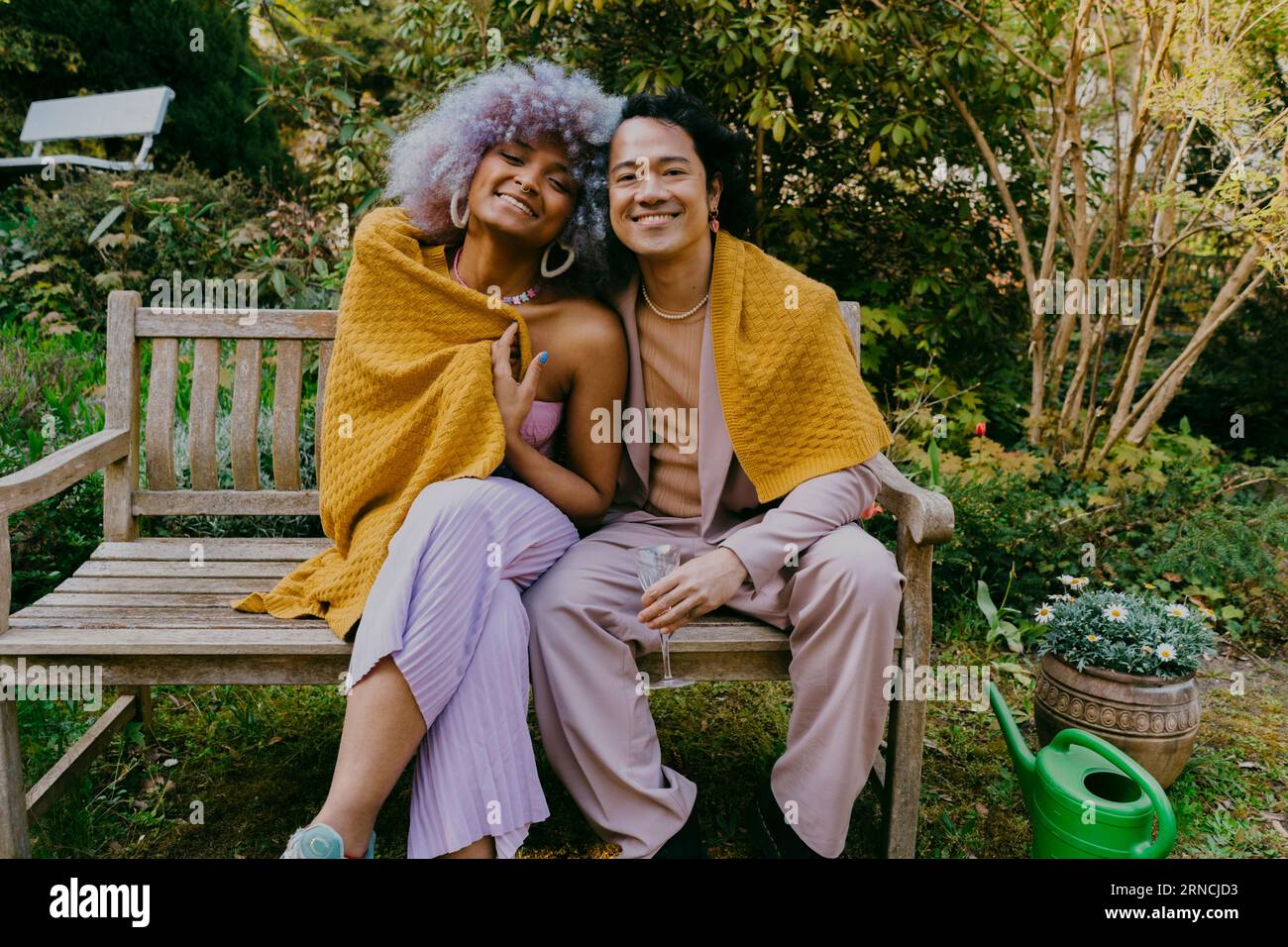 Porträt von lächelnden LGBTQ-Freunden, die während einer Dinnerparty im Hinterhof zusammen auf der Bank sitzen Stockfoto