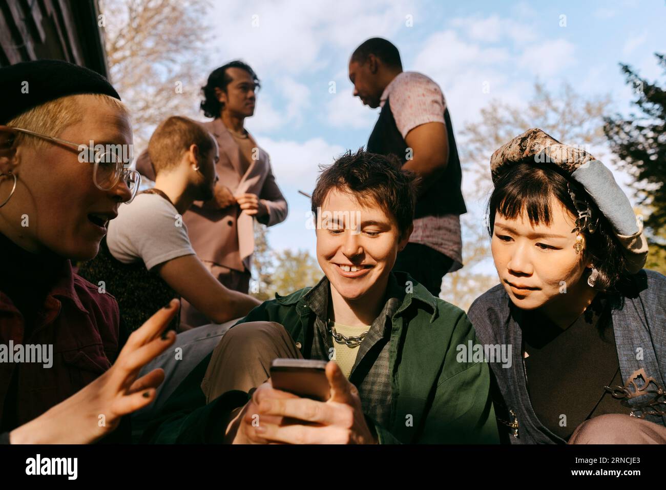 Neugierige LGBTQ-Freunde teilen ihr Smartphone während einer Dinnerparty im Hinterhof Stockfoto