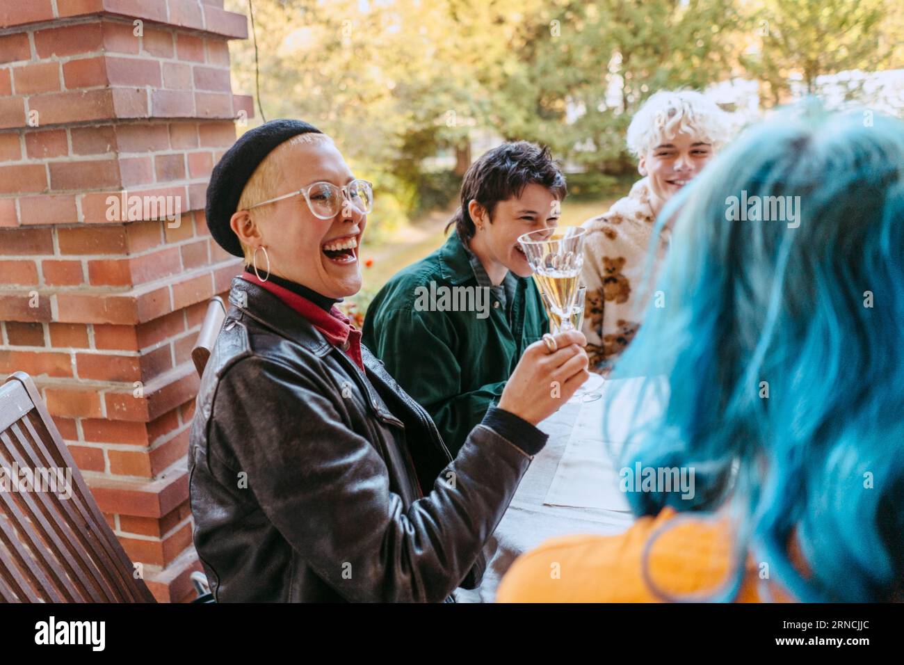 Seitenansicht der glücklichen schwulen Frau, die lachte, während sie Weinglas während der Dinnerparty im Hinterhof hielt Stockfoto