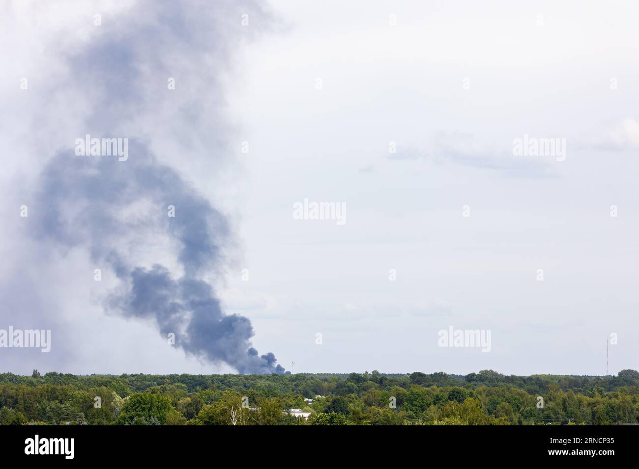 Schwarzer Rauch von einem Feuer, das über den Horizont steigt. Luftverunreinigung durch Umweltkatastrophe, die im Feuer endet. Foto aufgenommen an einem bewölkten Tag. Stockfoto