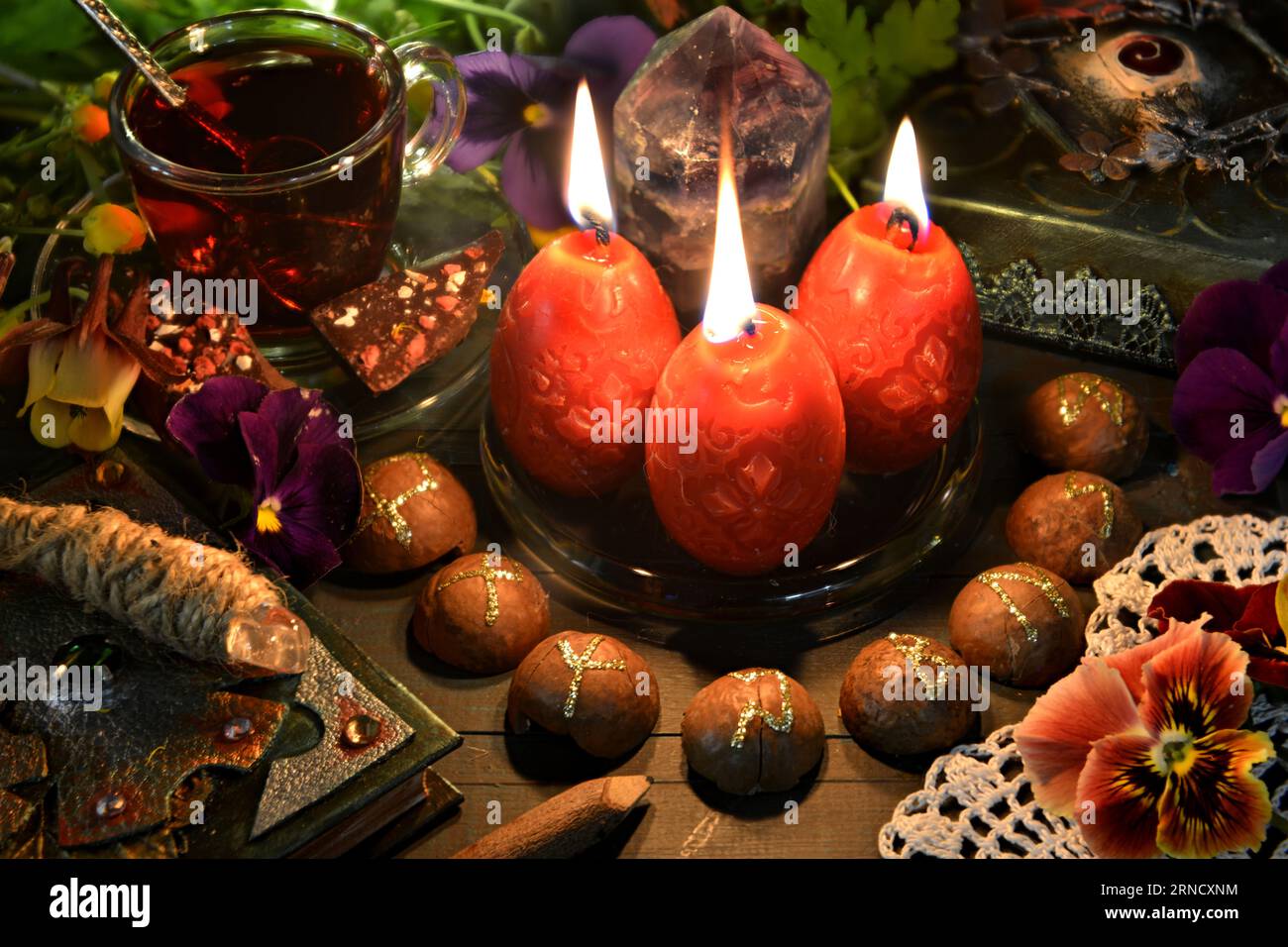 Stillleben mit roten Kerzen, Runen, Zauberstab und Zauberbuch auf dem rituellen Tisch. Okkultes, esoterisches und Hexenkonzept. Mystischer Hintergrund mit vin Stockfoto