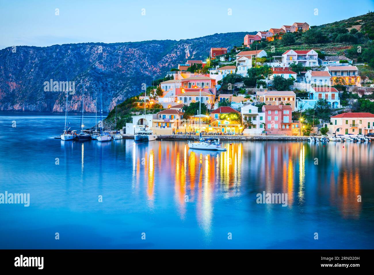 Assos, Griechenland. Wunderschönes Kefalonia, malerisches Dorf eingebettet auf den idyllischen Ionischen Inseln, bunte Häuser beleuchtet Dämmerung. Stockfoto
