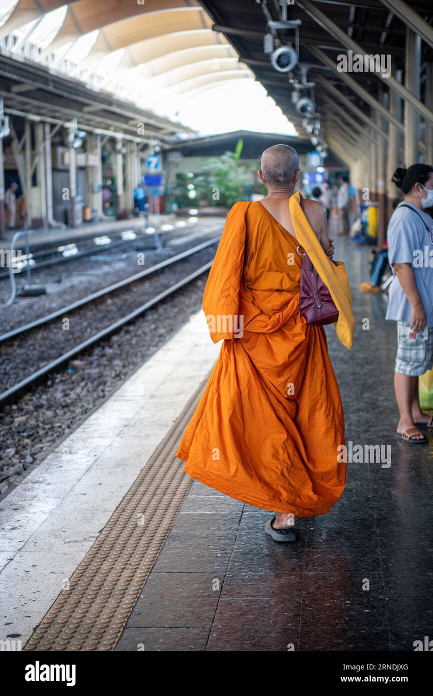 Dieses Foto wurde von hinten aufgenommen und zeigt einen buddhistischen Mönch in traditionellen orangen Gewändern, der langsam auf einer ruhigen Plattform bei Hua Lamphong spaziert. Stockfoto