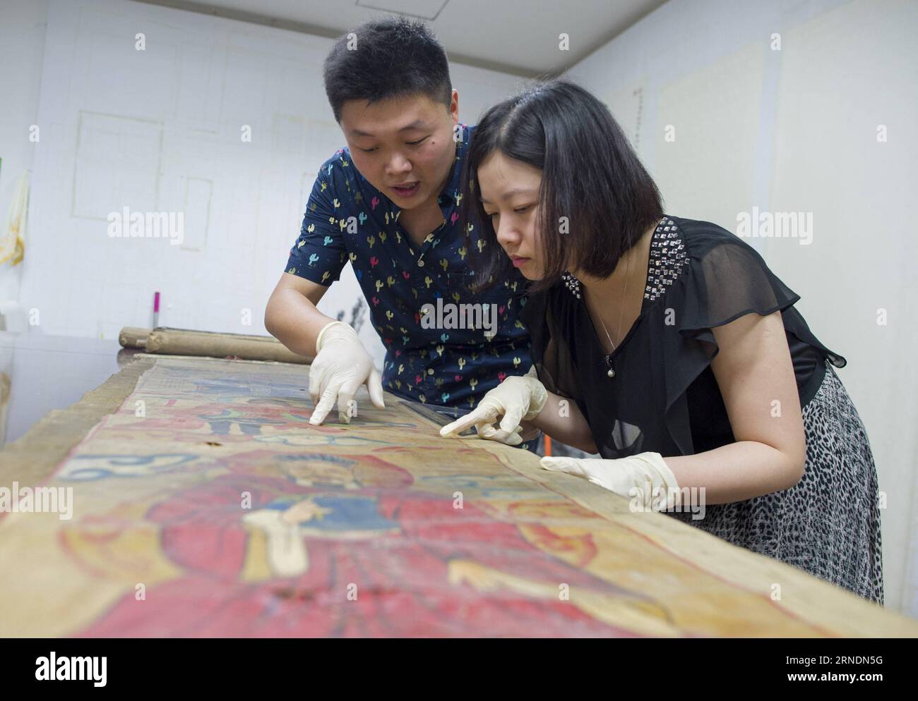 Zhao Xiaolong (L) stellt seiner Frau Zhang Xiaolong im Hubei Museum in Wuhan, der Hauptstadt der zentralchinesischen Provinz Hubei, am 16. Mai 2016 die Geschichte eines antiken Gemäldes vor. Zhang Xiaolong und Zhao Xiaolong, ein Paar, das in den 1980er Jahren geboren wurde, arbeiten beide an der Restaurierung kultureller Reliquien im Hubei Museum. Zhao und Zhang haben sich im gleichen Alter auf verschiedene berufliche Aspekte spezialisiert: Zhao widmet sich der Restaurierung kultureller Reliquien und Zhang ist gut in der Materialerkennung. Sie bauen ihre Beziehung durch Zusammenarbeit auf und bringen ihre Leidenschaft ein Stockfoto