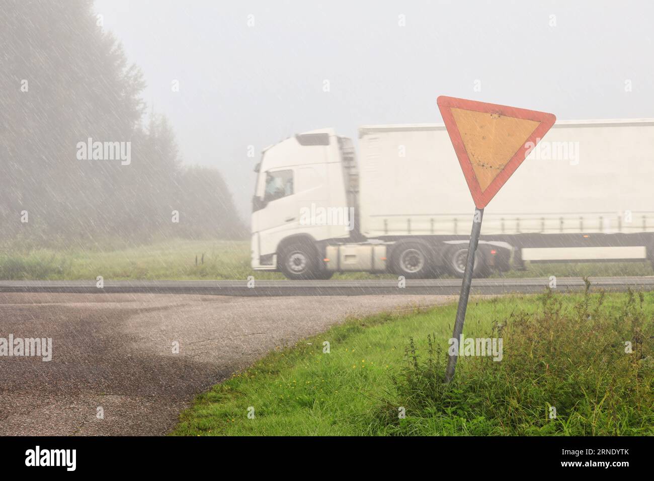Wegweiser auf einer Landstraße mit weißem Sattelauflieger, der an einem regnerischen, nebligen Tag mit geringer Sicht auf der Autobahn mit Geschwindigkeit vorbeifährt. Stockfoto