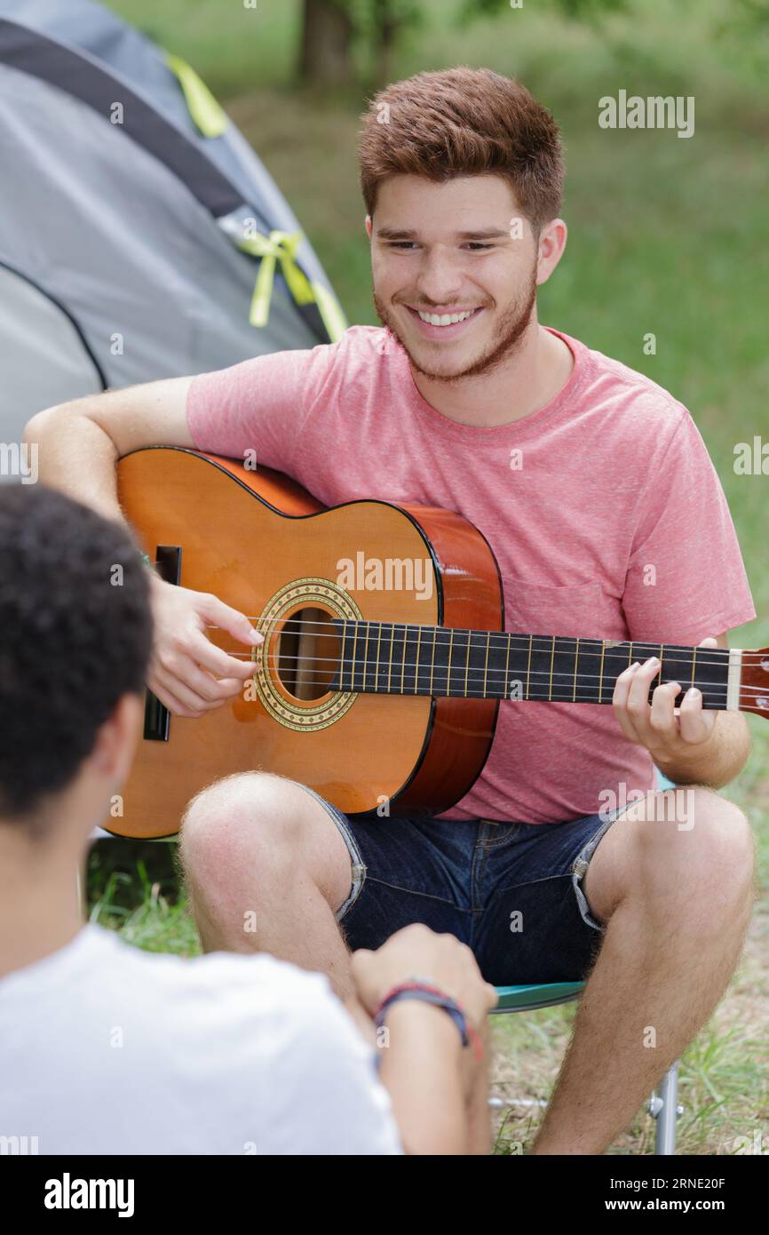 Mann, der vor dem Zelt singt und Gitarre spielt Stockfoto