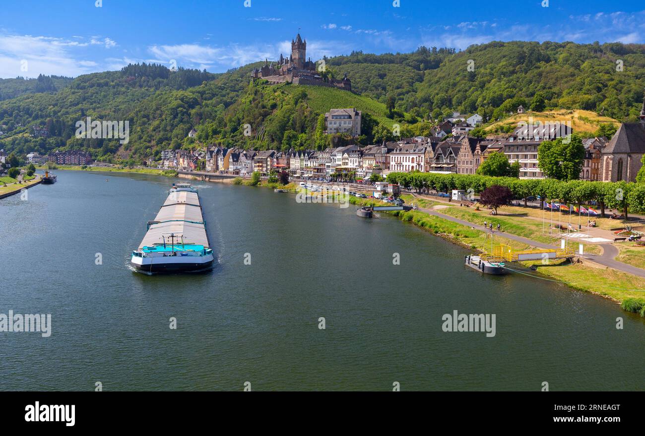 Ein selbstfahrendes Frachtschiff fährt an einem sonnigen Sommertag vor der Kulisse der Stadt Cochem entlang der Mosel. Deutschland Stockfoto