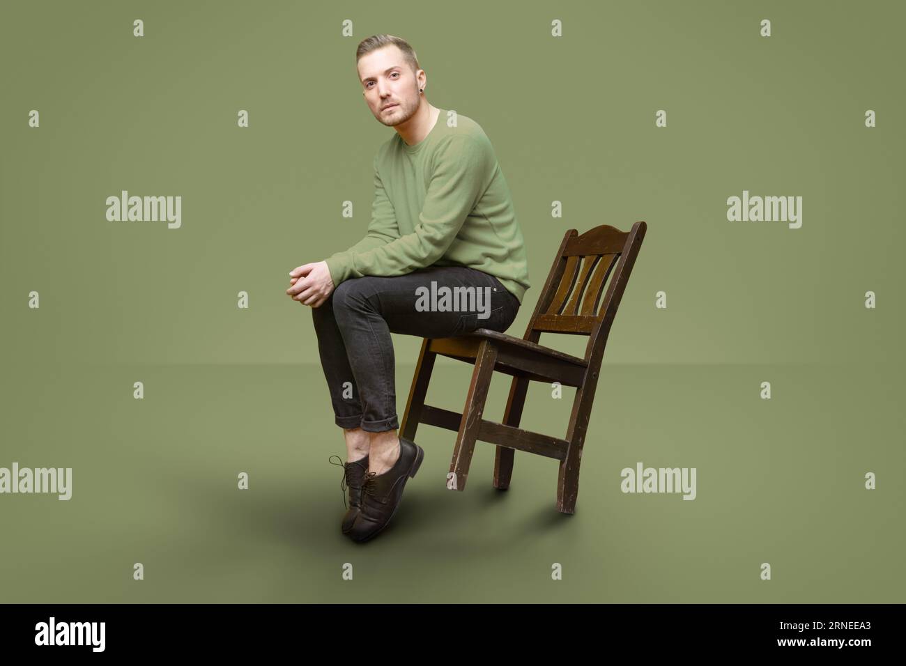 Gutaussehender Kerl, der sich mit dem Stuhl neigt, während er die Kamera anschaut und posiert Stockfoto