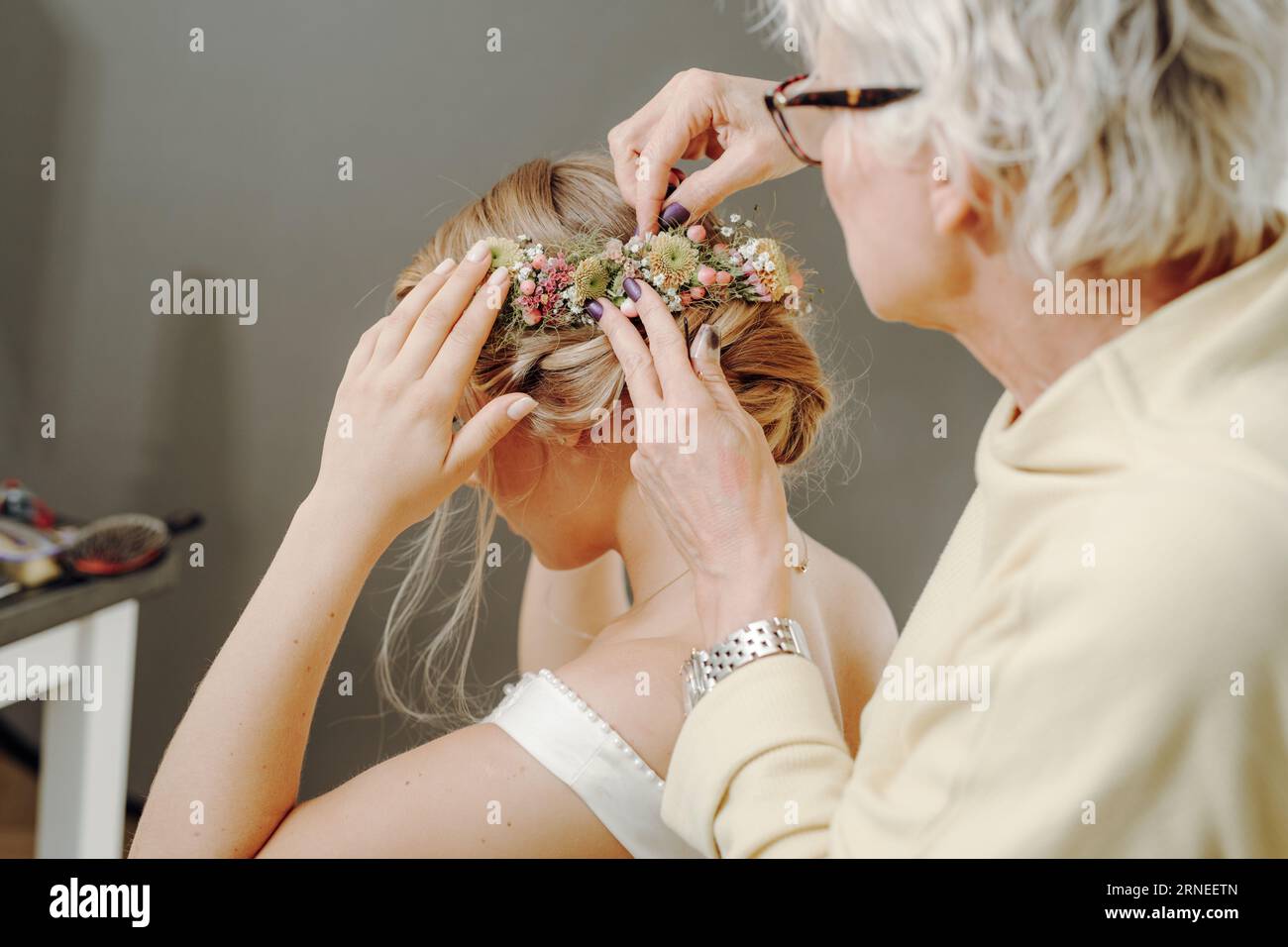 Braut Get ready with hair done from hairdresser with flowers and bouquet in updo Hair style while hairstylist pin flower to Head of Woman Stockfoto