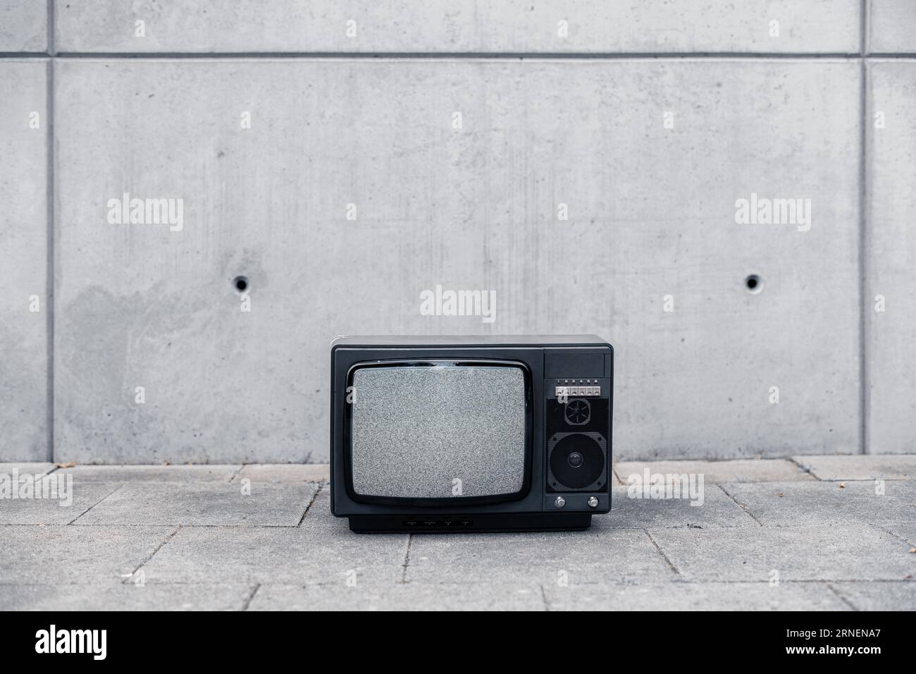 Alter Retro-tv-Stand draußen auf der Straße vor einer grundigenden Betonwand ohne Signal auf dem Bildschirm nur Lärm Stockfoto