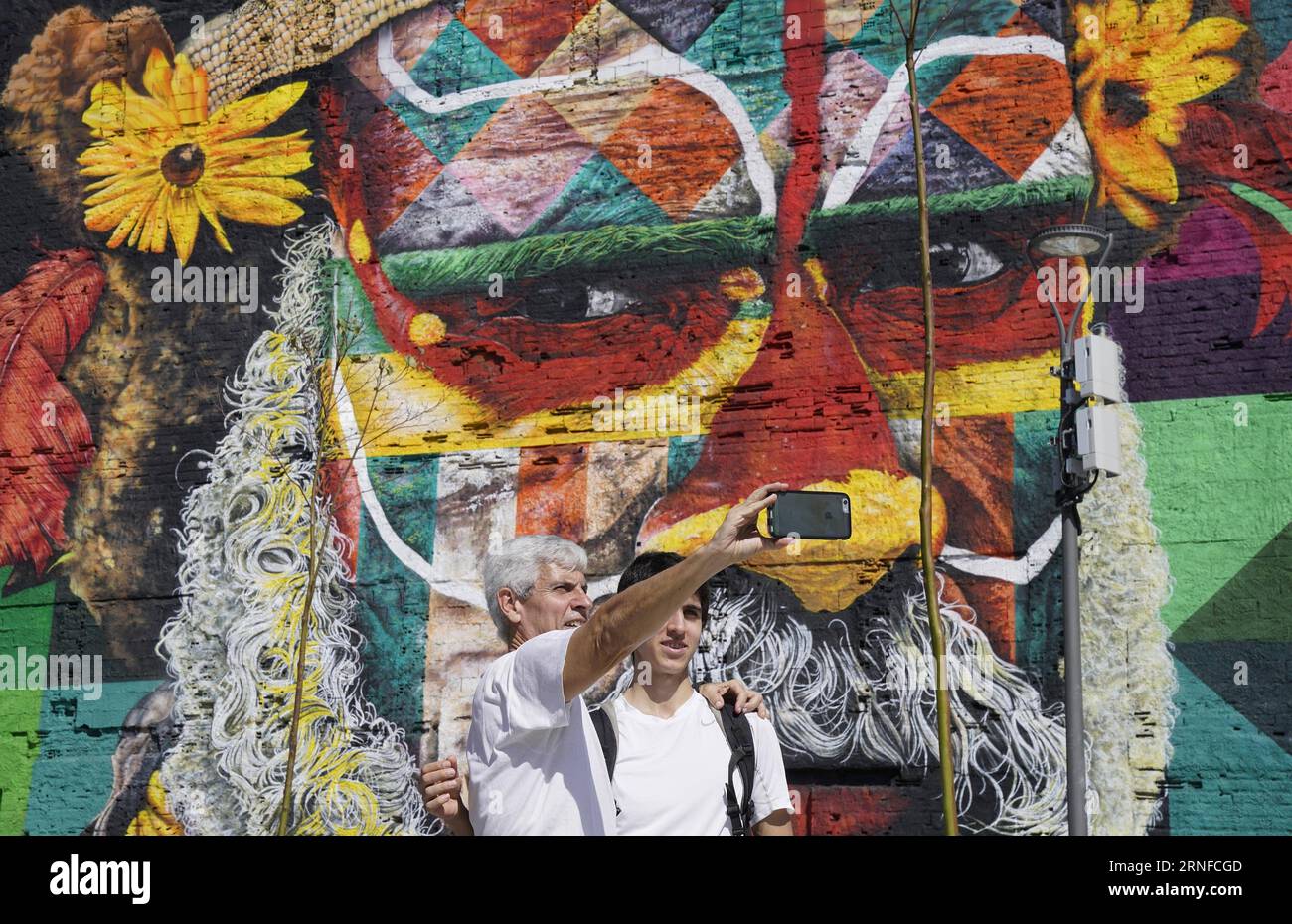 (160731) -- RIO DE JANEIRO, Juli 31,2016 -- Menschen nehmen Selfies vor einem riesigen Graffiti-Gemälde auf dem Olympic Boulevard in Rio de Janeiro, Brasilien, 31. Juli 2016. Der brasilianische Graffiti-Künstler Eduardo Kobra beendete das Gemälde Tage vor der Eröffnung der Olympischen Spiele in Rio 2016. Das Kunstwerk ist fast 3.000 Quadratmeter groß und zeigt einheimische Gesichter aus fünf Kontinenten.) (SP)BRASILIEN-RIO DE JANEIRO-OLYMPICS-GRAFFITI-GEMÄLDE WuxWei PUBLICATIONxNOTxINxCHN 160731 Rio de Janeiro Juli 31 2016 Prominente nehmen Selfies vor einem riesigen Graffiti-Gemälde AUF DEM Olympic Boulevard in Stockfoto