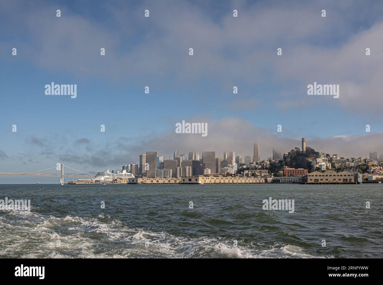 San Francisco, CA, USA - 12. Juli 2023: Finanzviertel hinter Hafendocks. Blick auf die Stadt vom grauen Wasser der Bucht unter der blauen Wolkenkulisse. SF-Oakland b Stockfoto