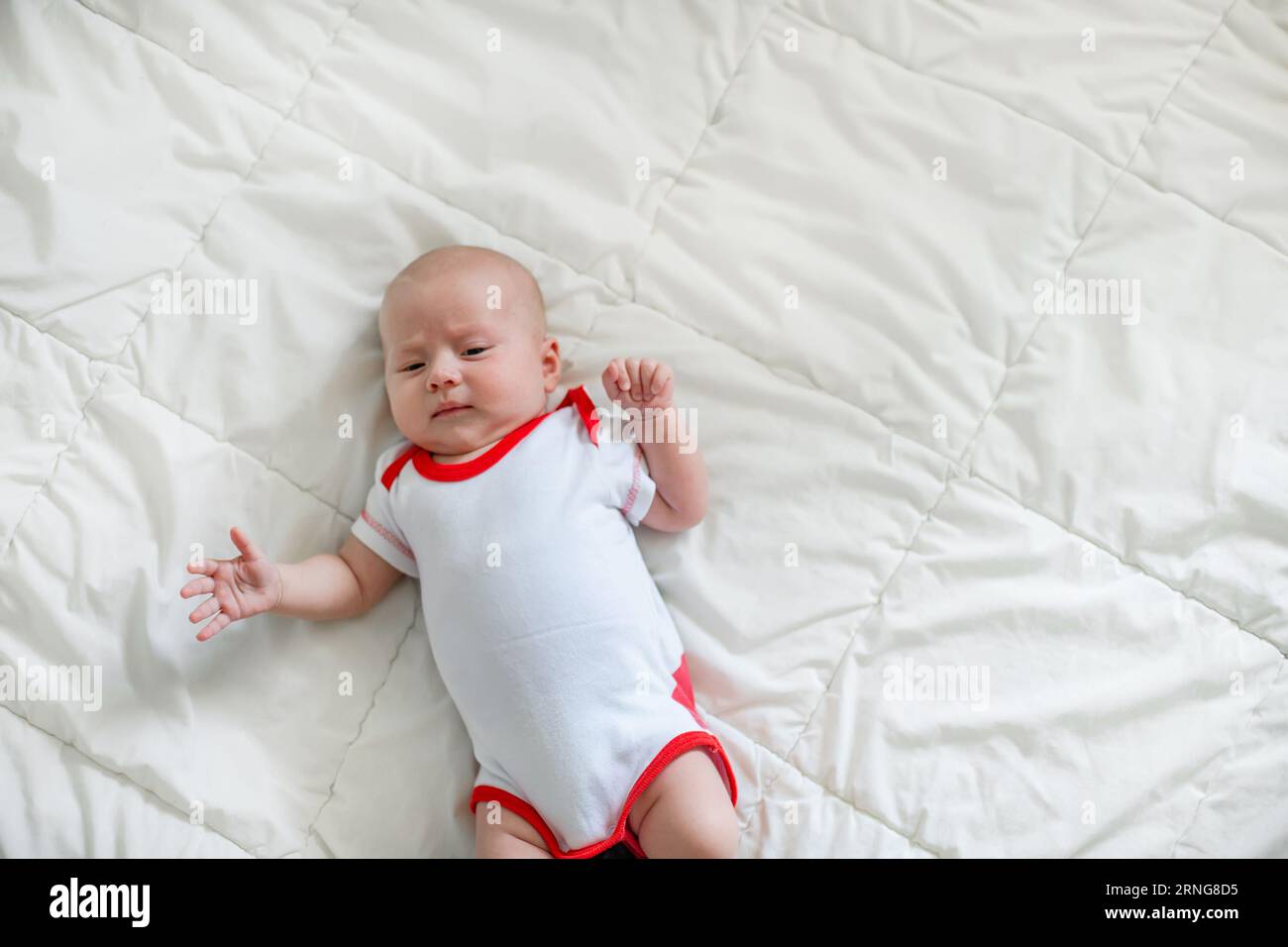 Ein kürzlich geborenes Baby, 2 Monate alt, lächelt glücklich auf dem Bett. Neu Gefundene Freude Stockfoto