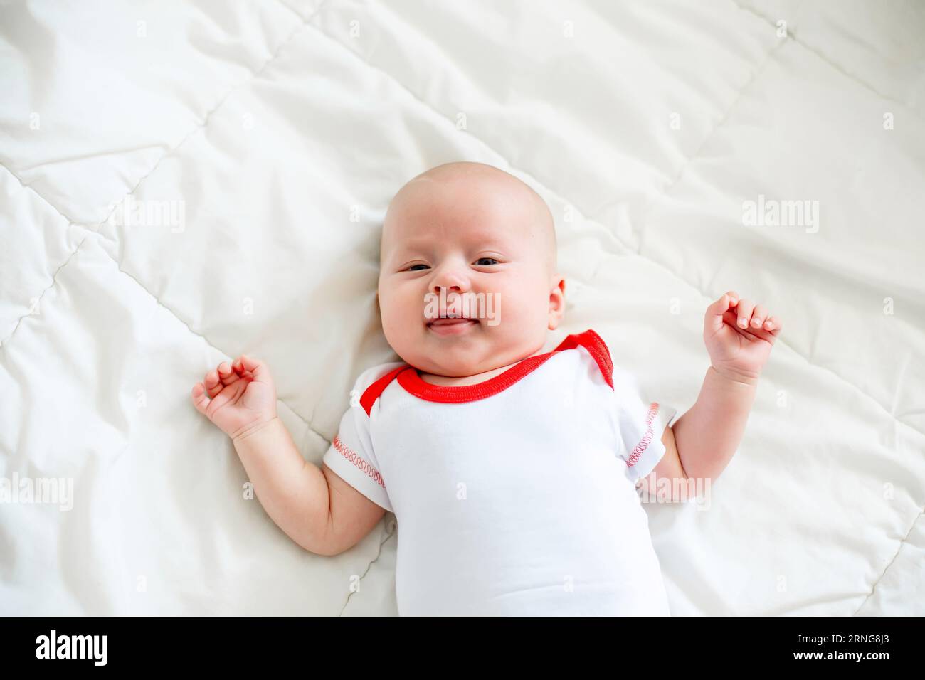Ein Neugeborenes liegt auf einer weißen Decke, die Arme sind seitlich ausgebreitet. Stockfoto