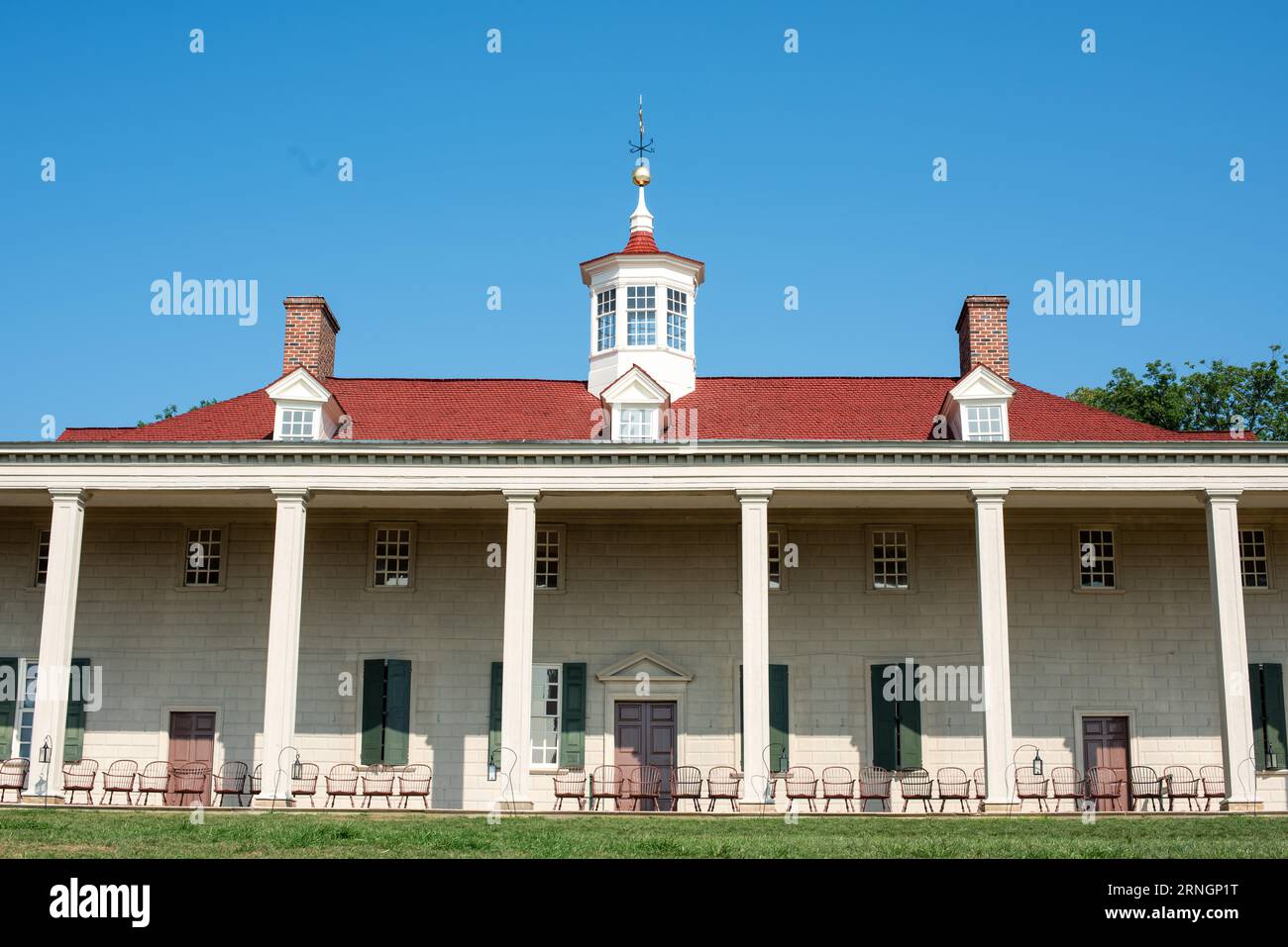 Mount Vernon Mansion mit Kolonnaden auf der Piazza Virginia // MOUNT VERNON, Virginia – das historische Mount Vernon Mansion, das ehemalige Wohnhaus von George Washington, steht vor einem klaren blauen Himmel. Die zweistöckige Holzstruktur, weiß gestrichen mit grünen Fensterläden, verfügt über eine unverwechselbare säulenplatte mit Blick auf den Potomac River. Mount Vernon diente von 1754 bis zu seinem Tod im Jahr 1799 als Residenz Washingtons. Das sorgfältig erhaltene Anwesen umfasst gut gepflegte Rasenflächen und Gärten rund um das Haupthaus. Dieses National Historic Landmark befindet sich etwa 24 km südlich von Washington Stockfoto