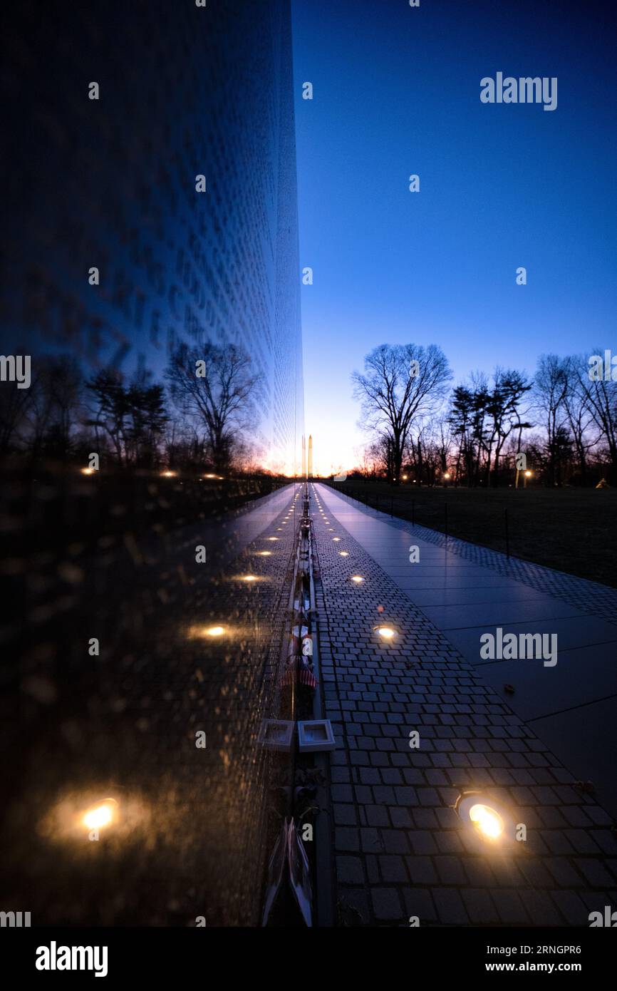 Vietnam Veterans Memorial Wall Washington DC // WASHINGTON DC – das Vietnam Veterans Memorial ist eine ergreifende Hommage an diejenigen, die im Vietnamkrieg gedient haben. Diese Mauer aus schwarzem Granit trägt die Namen von über 58.000 Soldaten, die entweder bei der Aktion getötet wurden oder vermisst bleiben. Das Denkmal dient als Ort der Reflexion und Erinnerung für Veteranen, Familien und Besucher gleichermaßen. In der Ferne befindet sich das Washington Monument. Stockfoto