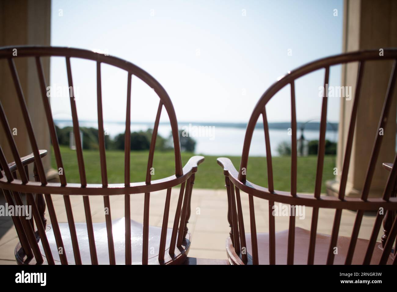 Mount Vernon Windsor Stühle Piazza View Virginia // MOUNT VERNON, Virginia - traditionelle Windsor Stühle aus Holz, die zu den Fensterläden grün gestrichen sind, säumen die ikonische säulenplatz auf George Washingtons Mount Vernon Anwesen. Die Stühle blicken nach außen zum weitläufigen Rasen und dem Potomac River dahinter und bieten dieselbe Sicht, die Amerikas erster Präsident genossen hätte. Mount Vernon diente von 1754 bis zu seinem Tod 1799 als Wohnhaus in Washington, und die piazza war eine spätere Ergänzung, die er in den 1770er Jahren selbst entwarf Diese historische Veranda ist ein Beispiel für den eleganten, aber praktischen Lebensstil Stockfoto