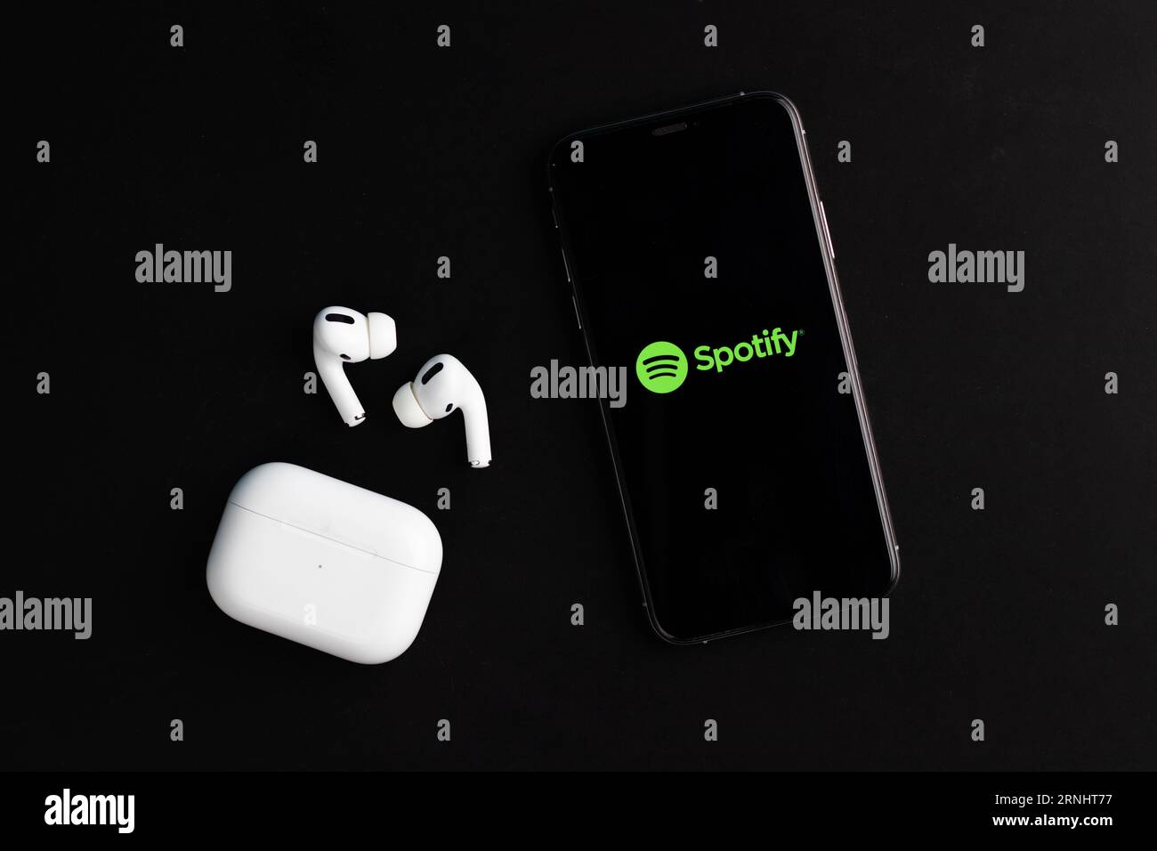 Spotify Logo auf dem Telefonbildschirm mit Airpods Pro auf dem Schreibtisch Stockfoto