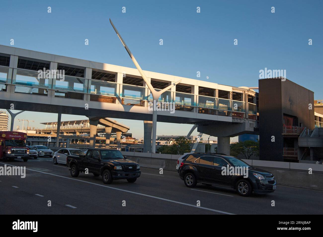 Der Autoverkehr auf der Ankunftsebene des LAX Airport verläuft unter einer Fußgängerbrücke mit dem neu installierten U-Bahnhof im Hintergrund. Stockfoto