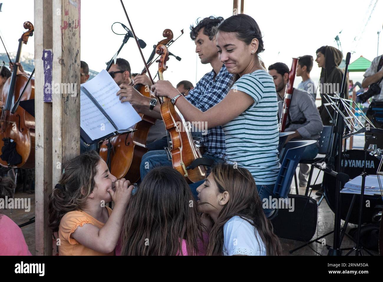 (170510) -- ATHEN, 10. Mai 2017 -- Flüchtlingskinder hören die Aufführung des Municipal Youth Orchestra of Caracas aus Venezuela im?Skaramangas Flüchtlingscamp in der Nähe von Piräus, Griechenland, am 10. Mai 2017. Die venezolanischen Musiker gaben ein Konzert im Flüchtlingscamp Skaramangas, dem größten staatlich geführten Flüchtlingscamp Griechenlands. Im Flüchtlingslager Skaramangas versuchen mehr als 3.500 Menschen, als Gemeinschaft zu fungieren und die täglichen Herausforderungen zu meistern, während sie darauf warten, in andere europäische Länder umgesiedelt zu werden. Das Lager wird von der griechischen Marine betrieben und von NGOs betrieben. Es befindet sich in einer riesigen Industriezone neben P Stockfoto