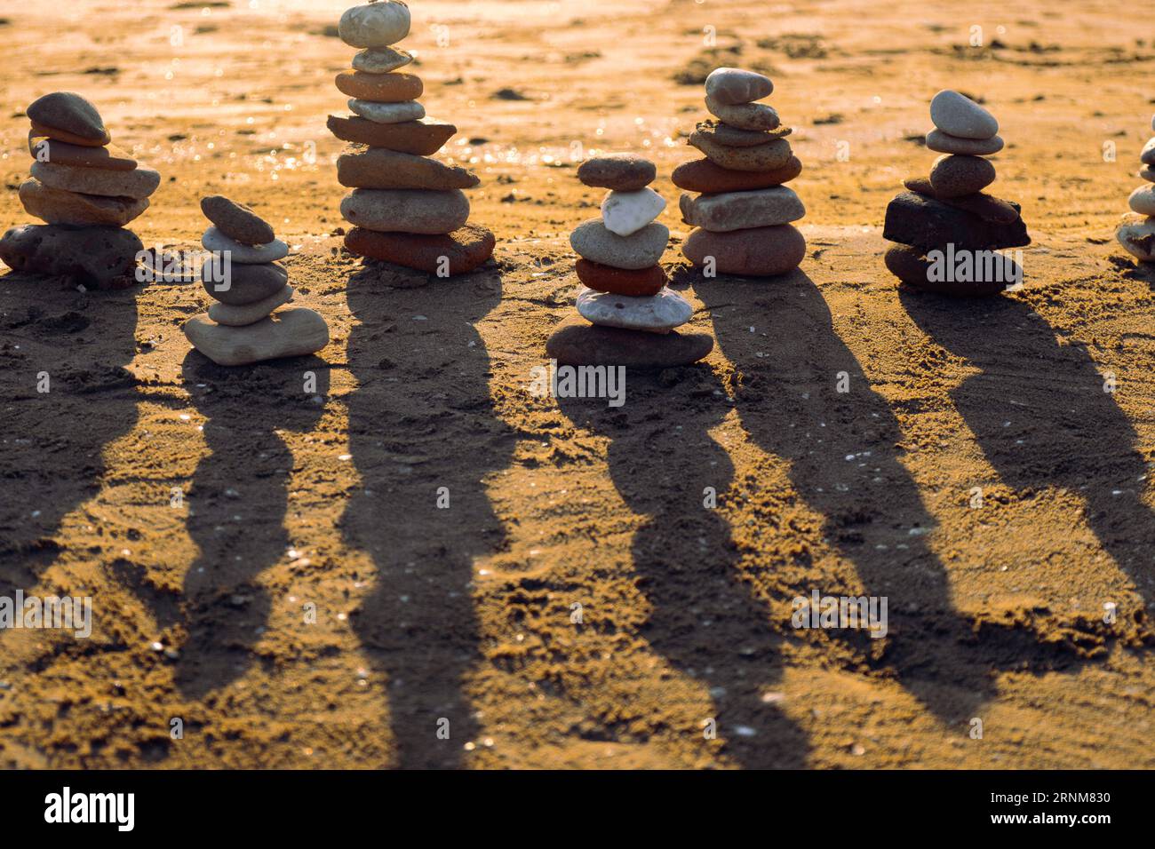 Ausgewogene Kieselpyramidensilhouette am Strand bei Sonnenuntergang mit Meer im Hintergrund. Zen Steine am Strand, Meditation, Spa, Harmonie, Ruhe, Stockfoto