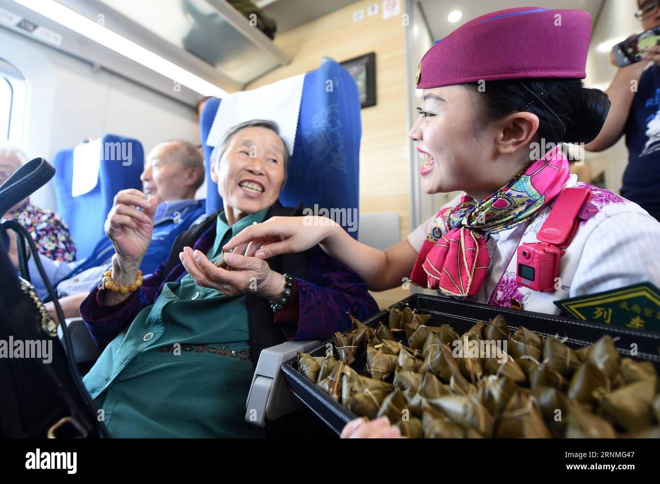 (170527) -- CHONGQING, 27. Mai 2017 -- Eine Stewardess serviert die zongzi, pyramidenförmige Knödel aus klebrigem Reis, umwickelt mit Bambus- oder Schilfblättern, für Passagiere in einem Hochgeschwindigkeitszug zwischen Chongqing und Chengdu im Südwesten Chinas, 27. Mai 2017. Zwischen Chengdu und Chongqing fand eine Party in mehreren Zügen statt, um das bevorstehende traditionelle Duanwu Festival oder das Dragon Boat Festival zu feiern, das am 30. Mai dieses Jahres stattfindet. (zhs) CHINA-CHONGQING-RAILWAY-DUANWU FESTIVAL (CN) TangxYi PUBLICATIONxNOTxINxCHN Chongqing Mai 27 2017 eine Stewardess dient der Zongzi Pyramid Shape Stockfoto