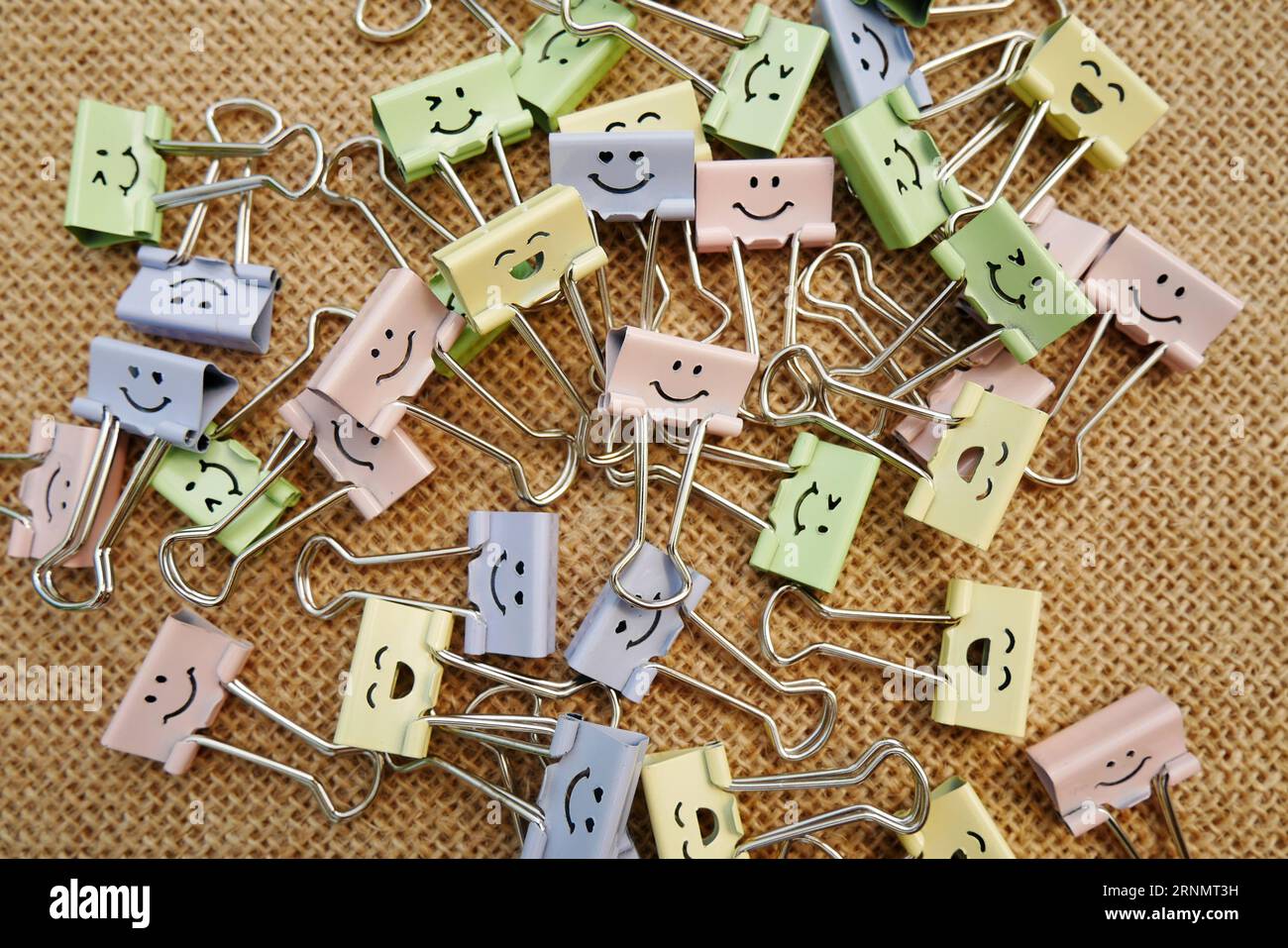 Pastellfarbene Büroklammern, Smiley Binder Clips und Stifte auf Notizblock. Bürobedarf auf ästhetischem Sackleinen-Hintergrund. Offenes Spiral-Notizbuch o Stockfoto
