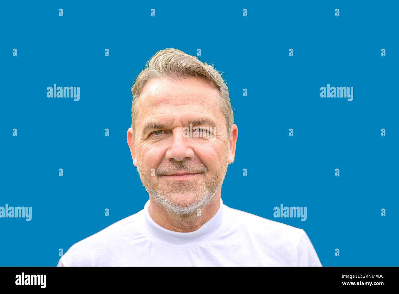 Close Up Porträt eines attraktiven Mannes mittleren Alters in seinen fünfziger Jahren mit einem sanften Lächeln vor einem blauen Hintergrund Stockfoto