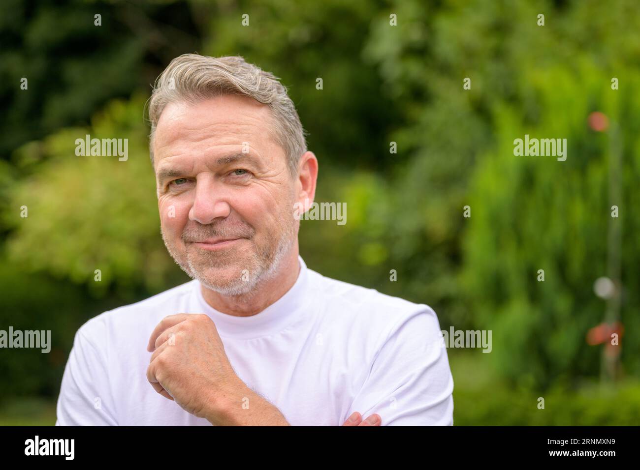 Nahaufnahme eines attraktiven Mannes mittleren Alters in seinen fünfziger Jahren mit einem schelmischen Lächeln, während er im Garten steht Stockfoto
