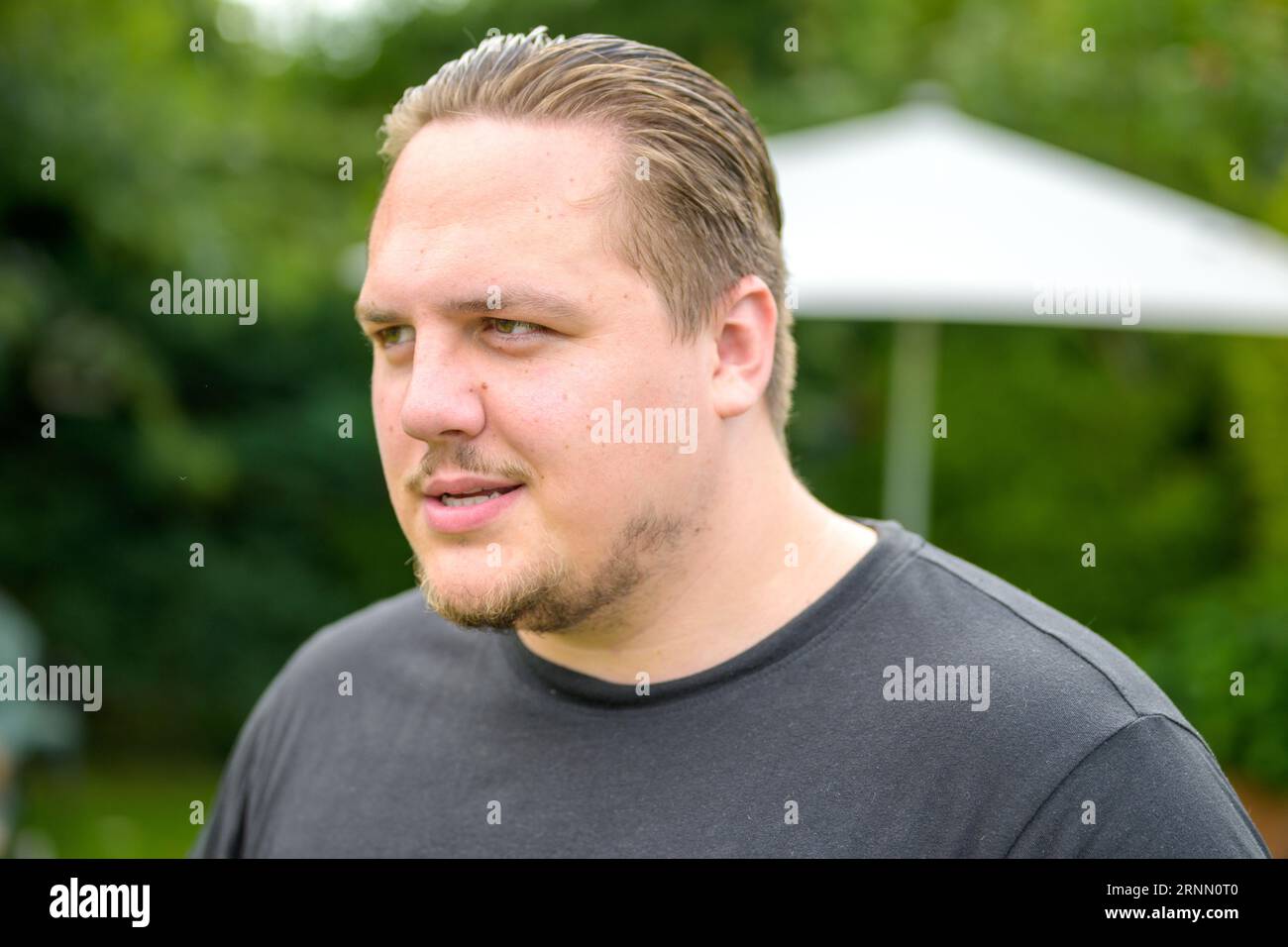 Der junge Mann in den Zwanzigern sieht freundlich seitwärts aus, während er im Garten steht Stockfoto