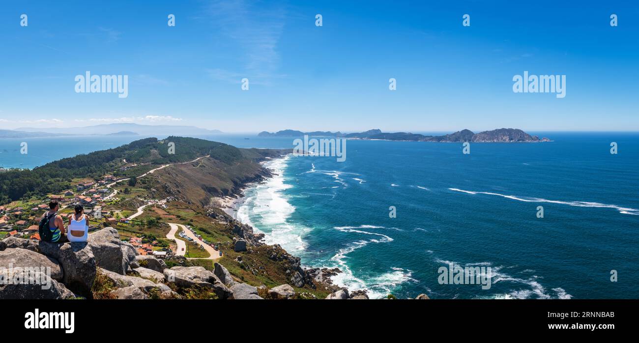 PONTEVEDRA, SPANIEN - 20. AUGUST 2023: Ein junges Paar genießt die Aussicht auf die schroffen Klippen von Cabo Home und die fernen Cies-Inseln am Ende des Stockfoto
