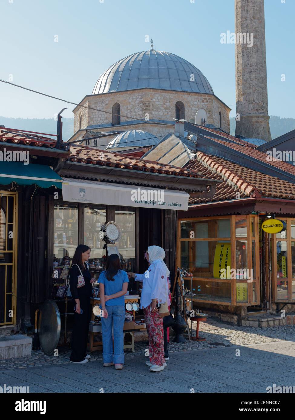 Freunde unterhalten sich vor einem Geschäft mit einer Moschee dahinter in Sarajevo, Bosnien und Herzegowina, am 2. September 2023 Stockfoto