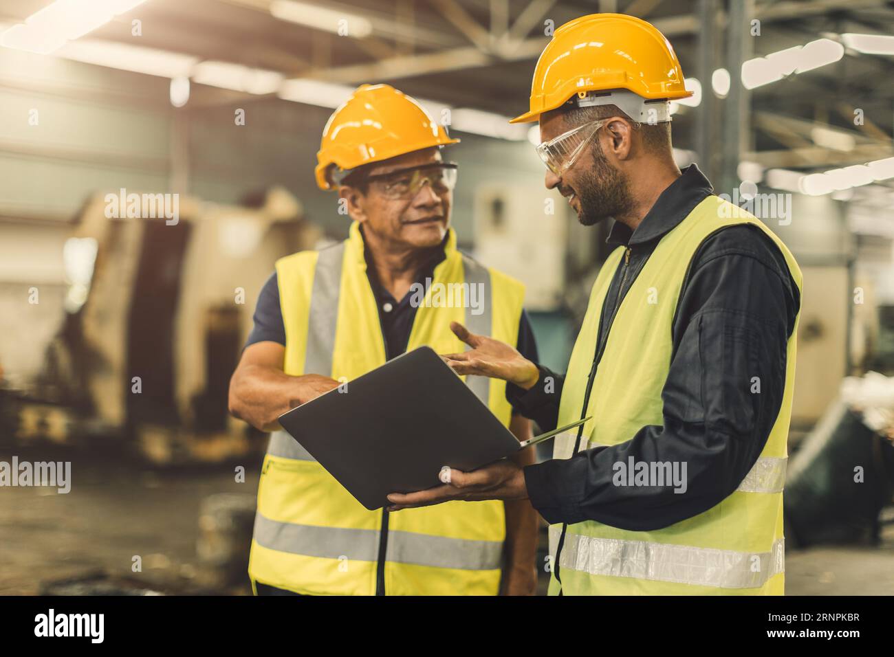 Asiatische männliche Arbeiter arbeiten zusammen, sprechen in einer Fabrik der Schwerindustrie Stockfoto
