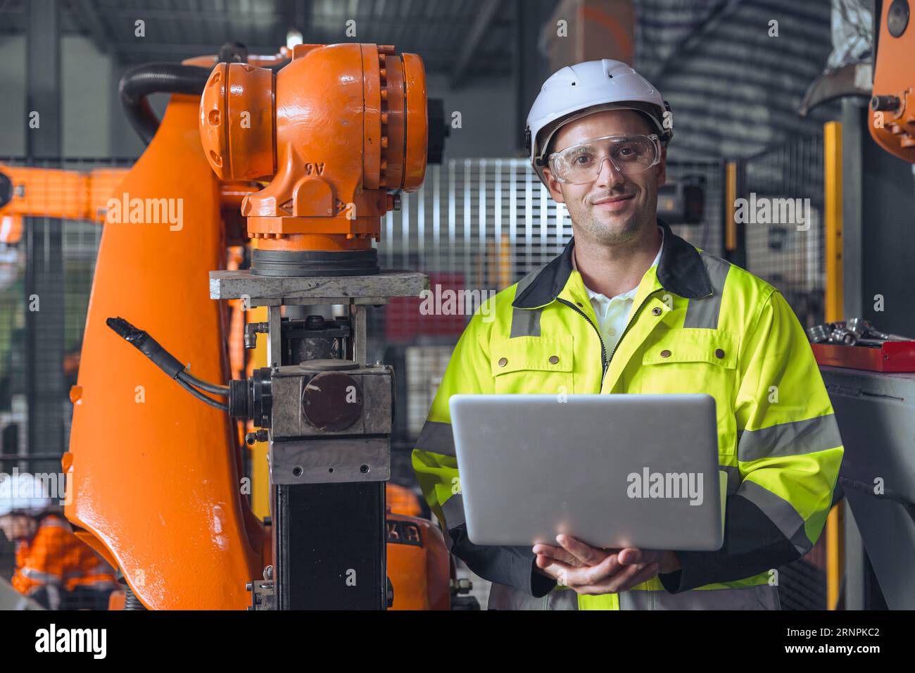 Porträt glücklicher Ingenieur männlich mit Laptop-Computer-Steuerung bedienen Industrie-Roboter Arm Maschine. Man Programmierservice Schweißroboter in Auto Stockfoto