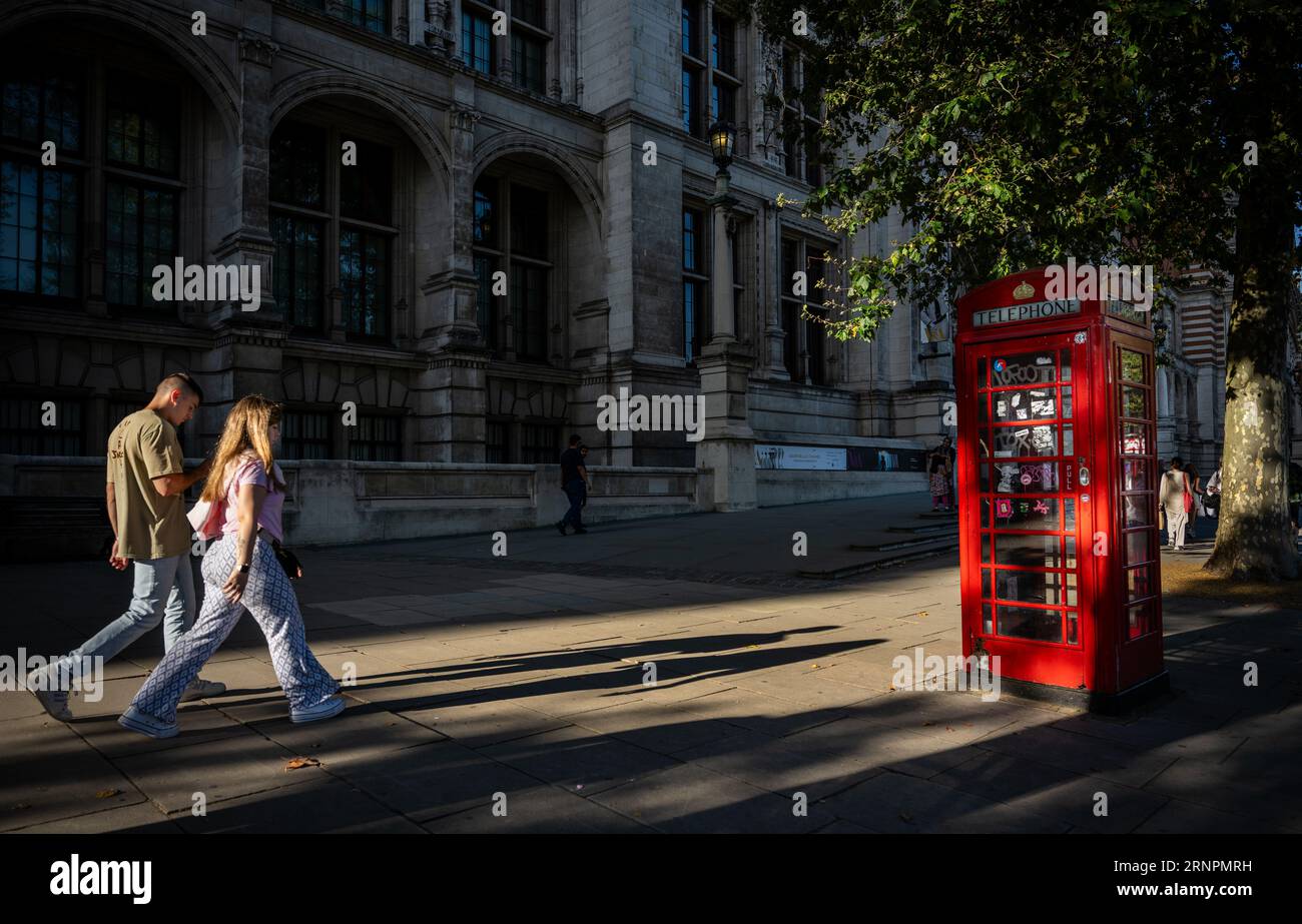 London, Großbritannien: Menschen, die auf dem Bürgersteig spazieren gehen und die Abendsonne lange Schatten wirft. Vor dem Victoria and Albert Museum in South Kensington. Stockfoto