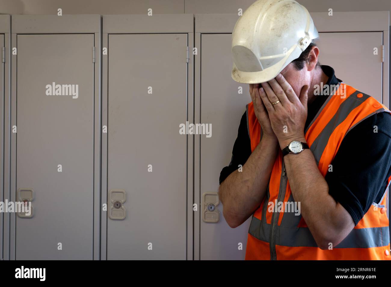 Ein männlicher Mitarbeiter mit dem Kopf in den Händen in der Verzweiflung, der in einer Industrie- oder Bauumgebung in einer psychischen Gesundheit zu kämpfen hat Stockfoto