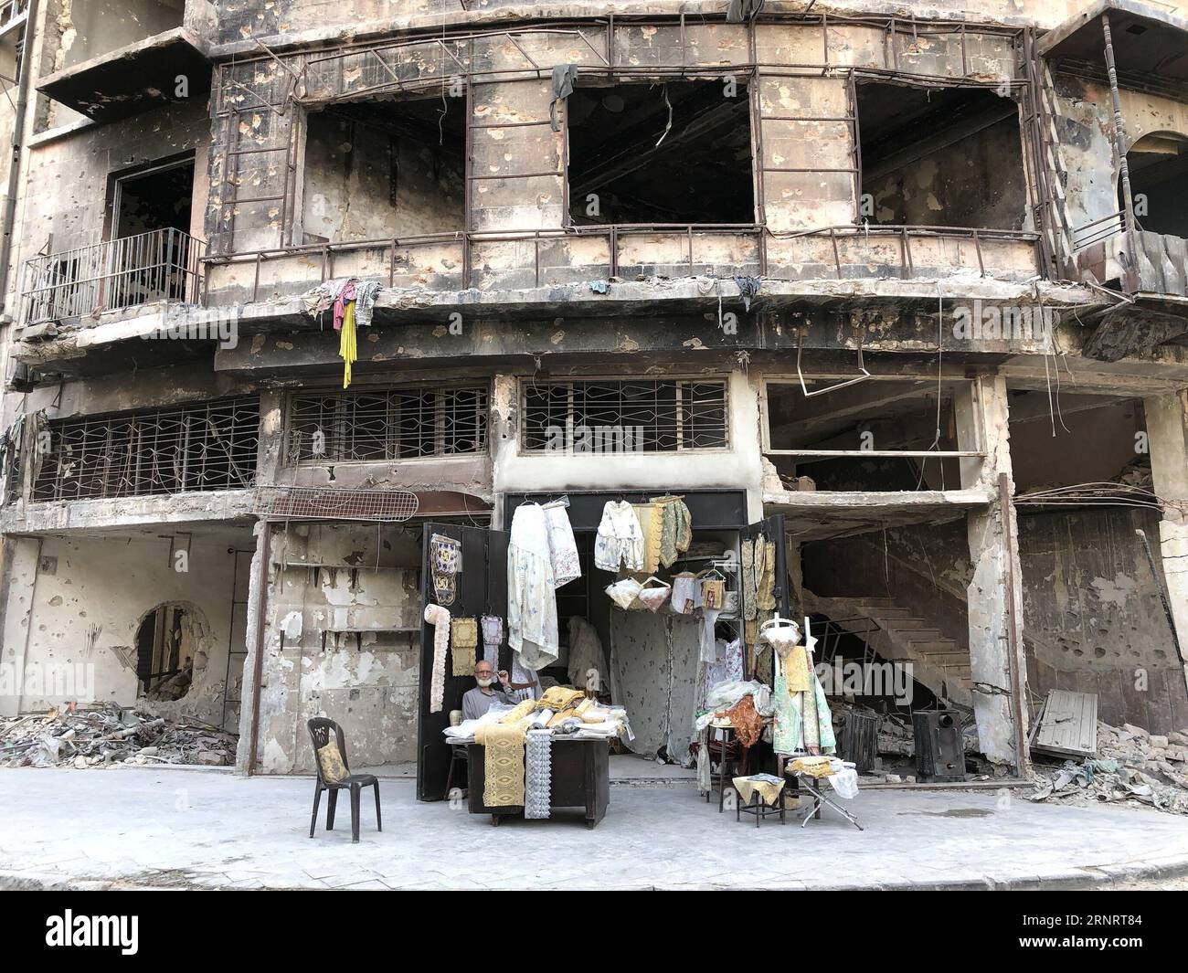 (171014) -- ALEPPO, 14. Oktober 2017 -- Abu Subhi sitzt am 12. Oktober 2017 vor seinem Geschäft in Aleppo, Syrien. In den Ruinen der historischsten Souks der Welt betreibt der 62-jährige Abu Subhi ein sehr kleines Geschäft in der Khan al-Harir-Straße in der alten Stadt Aleppo, umgeben von der Zerstörung des Krieges. Sein kleines Geschäft, in dem er Tischläufer und Tischdecken verkauft, ist das einzige Zeichen des Lebens in der Jahrhunderte alten Gegend.) SYRIEN-ALEPPO-ALTER KAUFMANN HummamxSheikhxAli PUBLICATIONxNOTxINxCHN Stockfoto