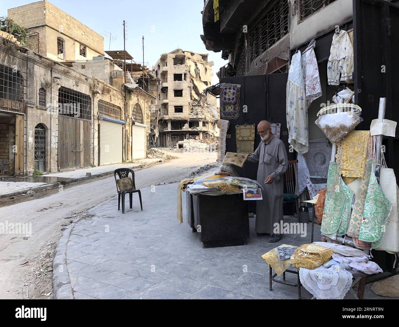 (171014) -- ALEPPO, 14. Oktober 2017 -- Abu Subhi arbeitet am 12. Oktober 2017 in seinem Geschäft in Aleppo, Syrien. In den Ruinen der historischsten Souks der Welt betreibt der 62-jährige Abu Subhi ein sehr kleines Geschäft in der Khan al-Harir-Straße in der alten Stadt Aleppo, umgeben von der Zerstörung des Krieges. Sein kleines Geschäft, in dem er Tischläufer und Tischdecken verkauft, ist das einzige Zeichen des Lebens in der Jahrhunderte alten Gegend.) SYRIEN-ALEPPO-ALTER KAUFMANN HummamxSheikhxAli PUBLICATIONxNOTxINxCHN Stockfoto